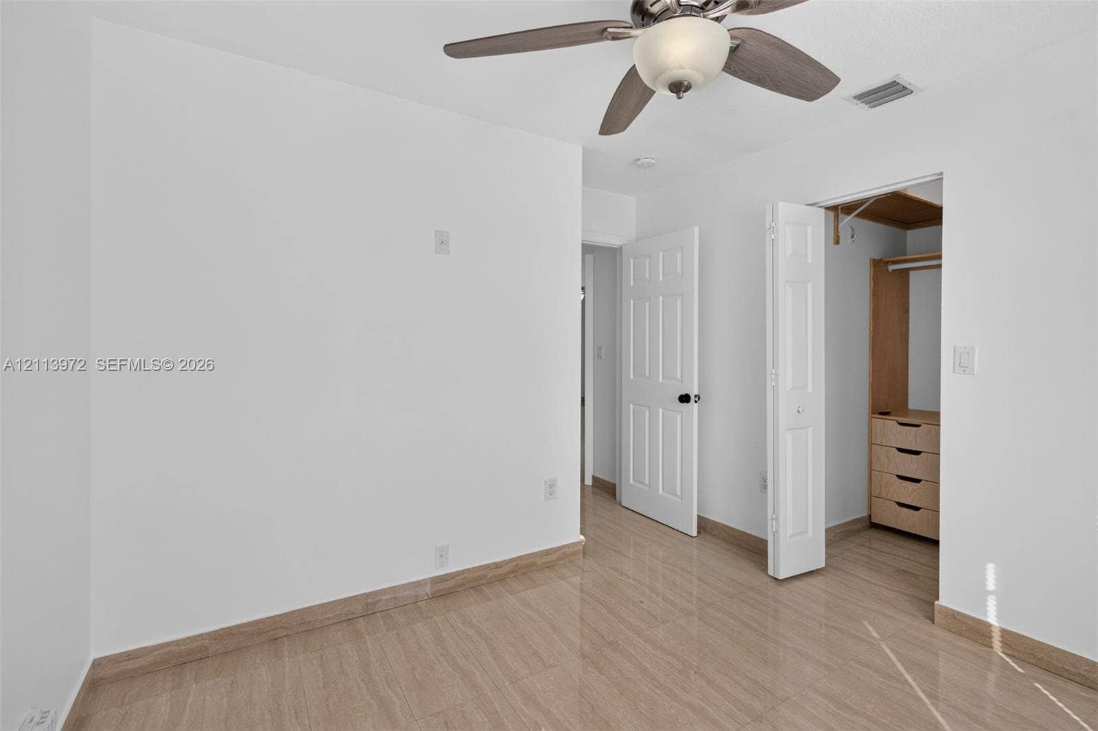 Neutral-toned space featuring polished tile flooring, a multi-blade ceiling fan with integrated lighting, and a closet with built-in wood-finish shelving and drawers
