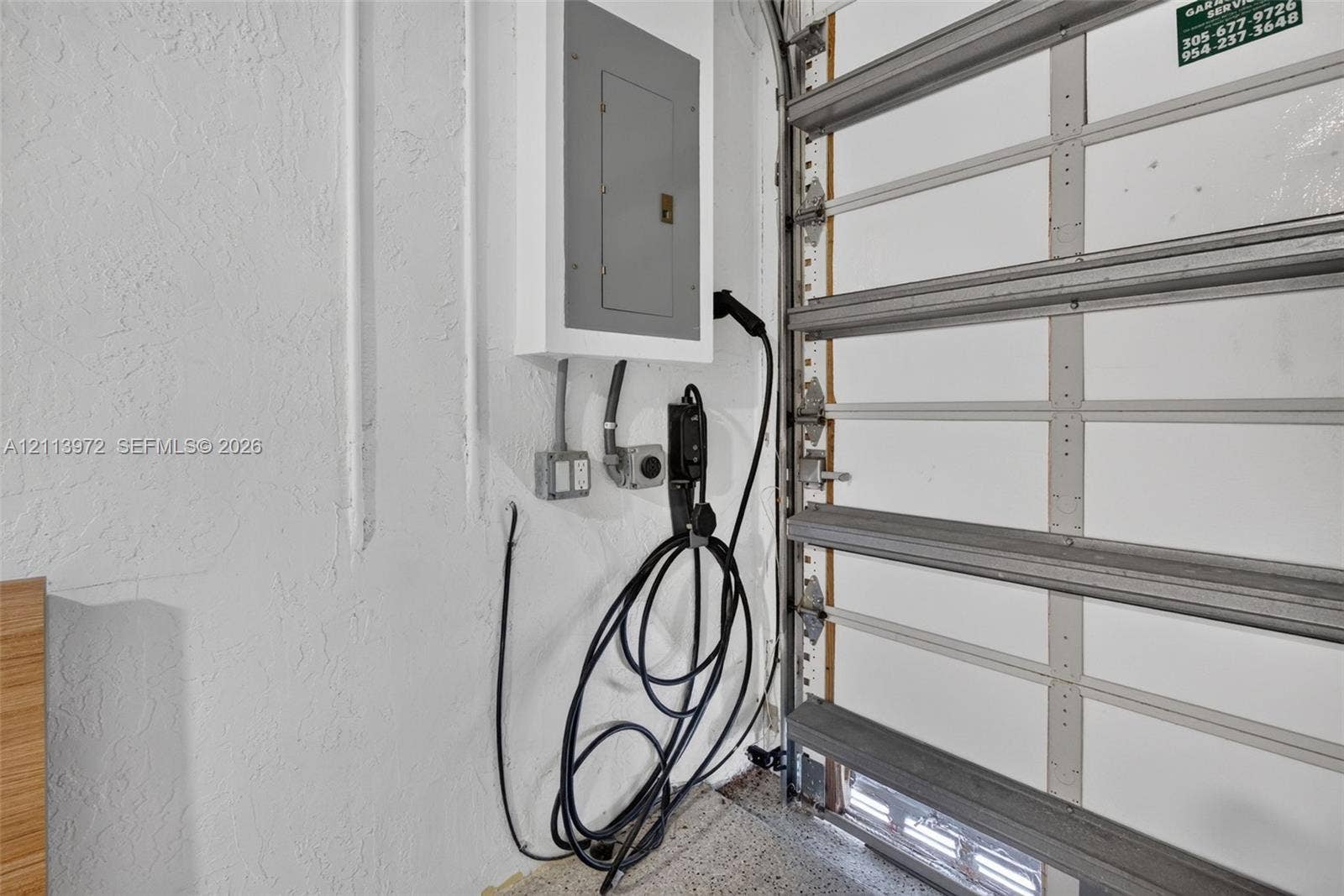 Garage interior featuring a dedicated electric vehicle charging station, surface-mounted electrical panel, and sectional overhead door