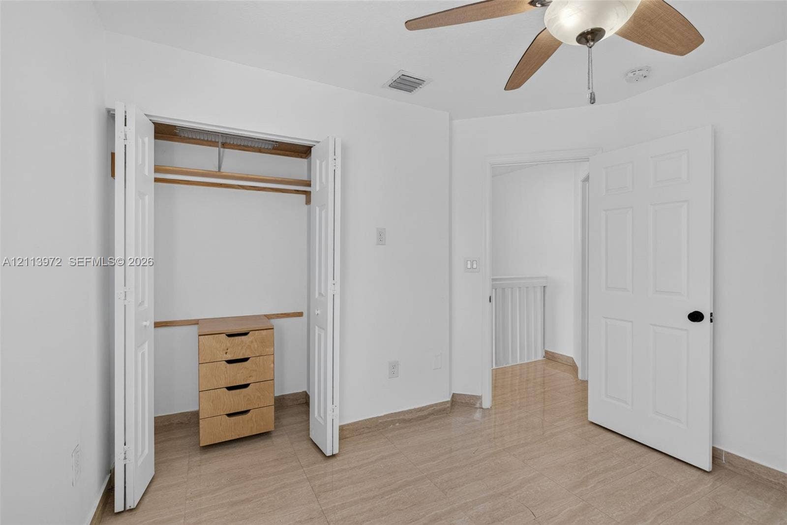 Neutral-toned tile flooring, bi-fold closet doors, built-in wooden drawer unit, and ceiling fan with integrated lighting