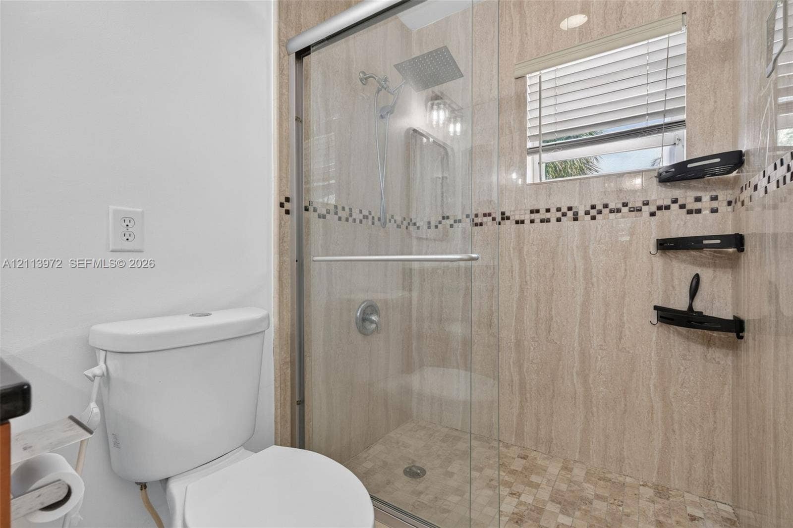 Walk-in shower featuring floor-to-ceiling stone-finish tile, a rainfall showerhead, glass sliding enclosure, and a decorative mosaic tile accent band