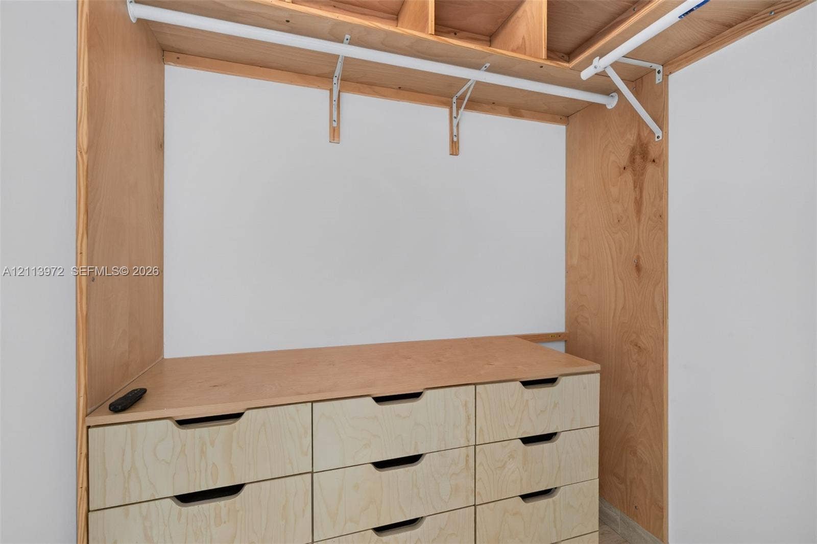 Custom-built storage featuring light wood cabinetry, integrated drawer units, open shelving, and white metal garment rods