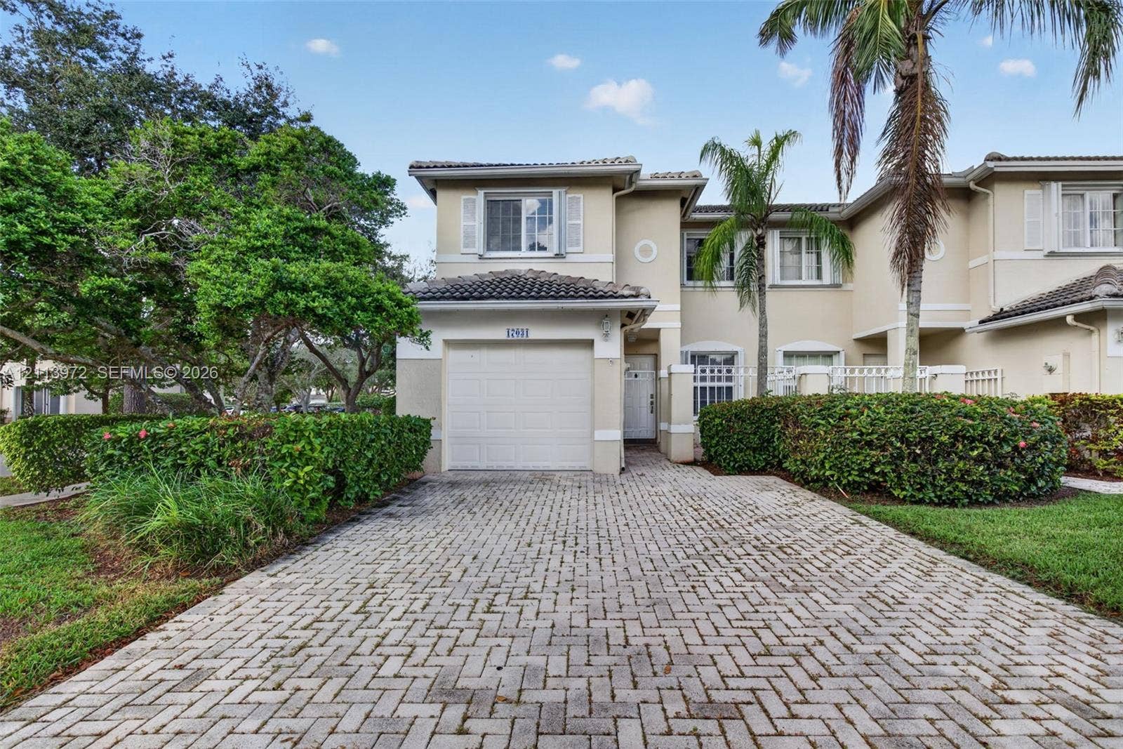 Two-story exterior featuring a stucco facade, tiled roof, attached single-car garage, and paved herringbone-pattern driveway