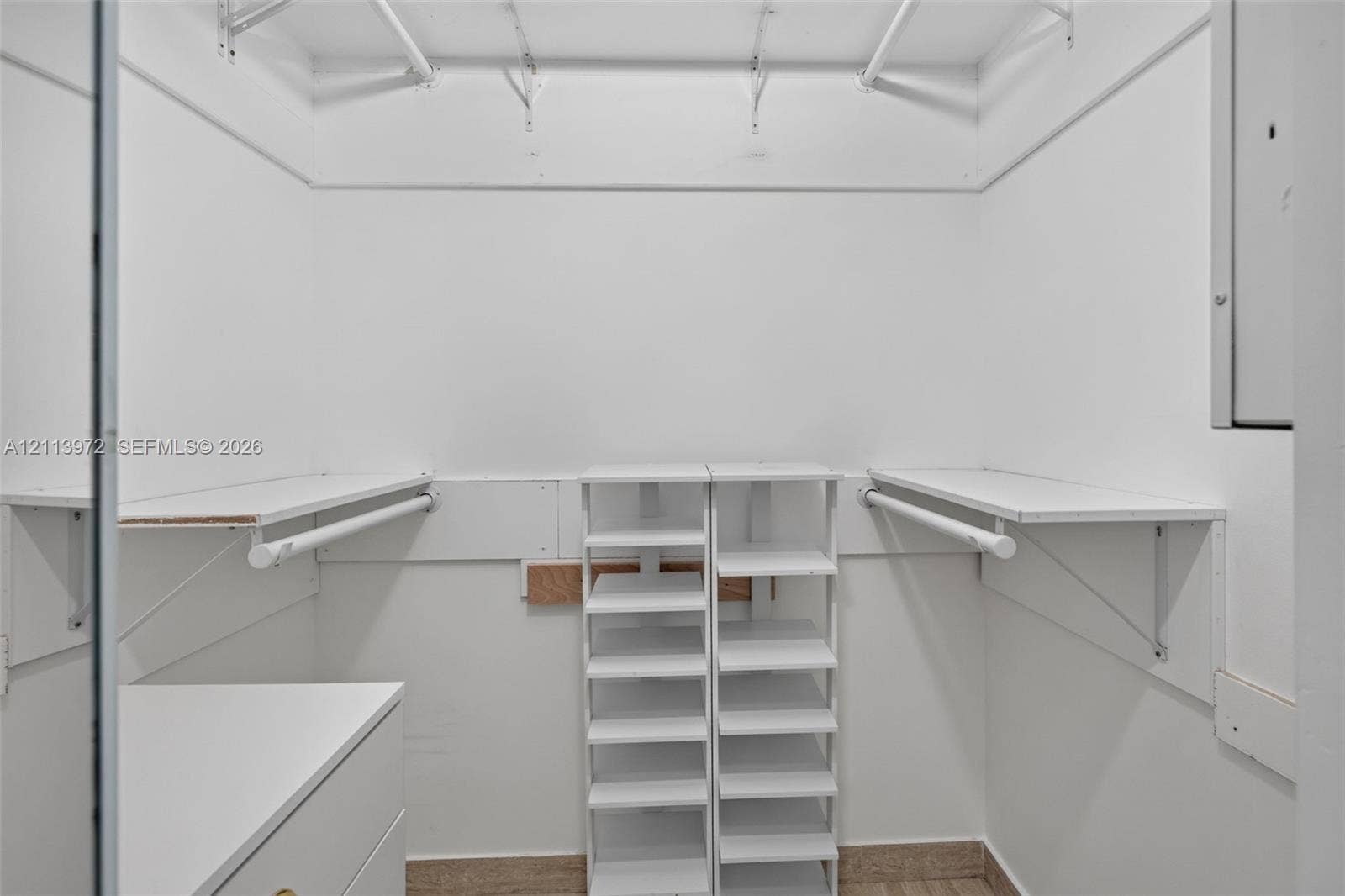 Walk-in closet featuring white built-in shelving, dual hanging rods, a tiered shoe rack, and wood-finish flooring