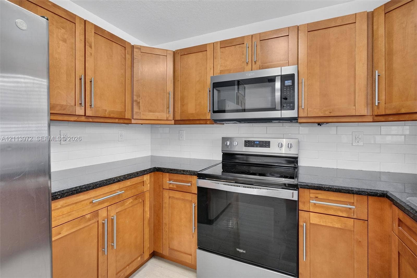 Kitchen featuring wood cabinetry, stainless steel appliances, dark stone-finish countertops, and a white subway tile backsplash