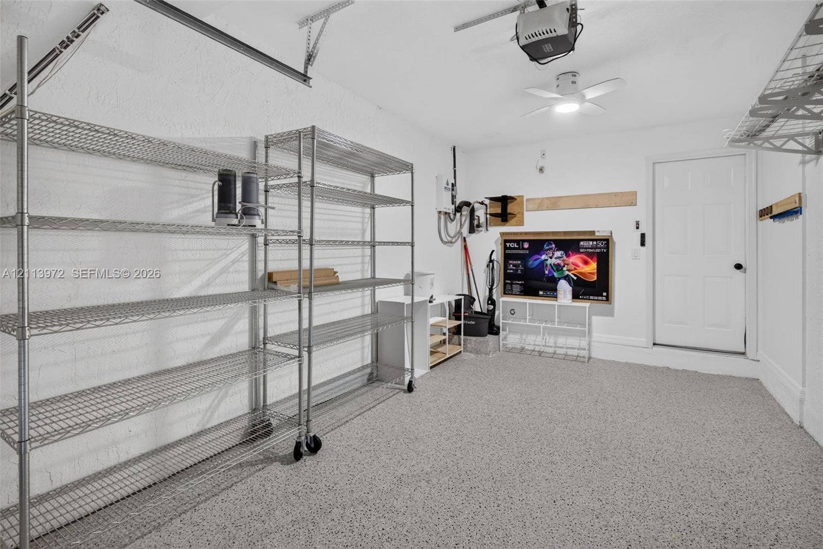 Garage space featuring epoxy flooring, textured walls, ceiling-mounted light fixture, and overhead storage shelving