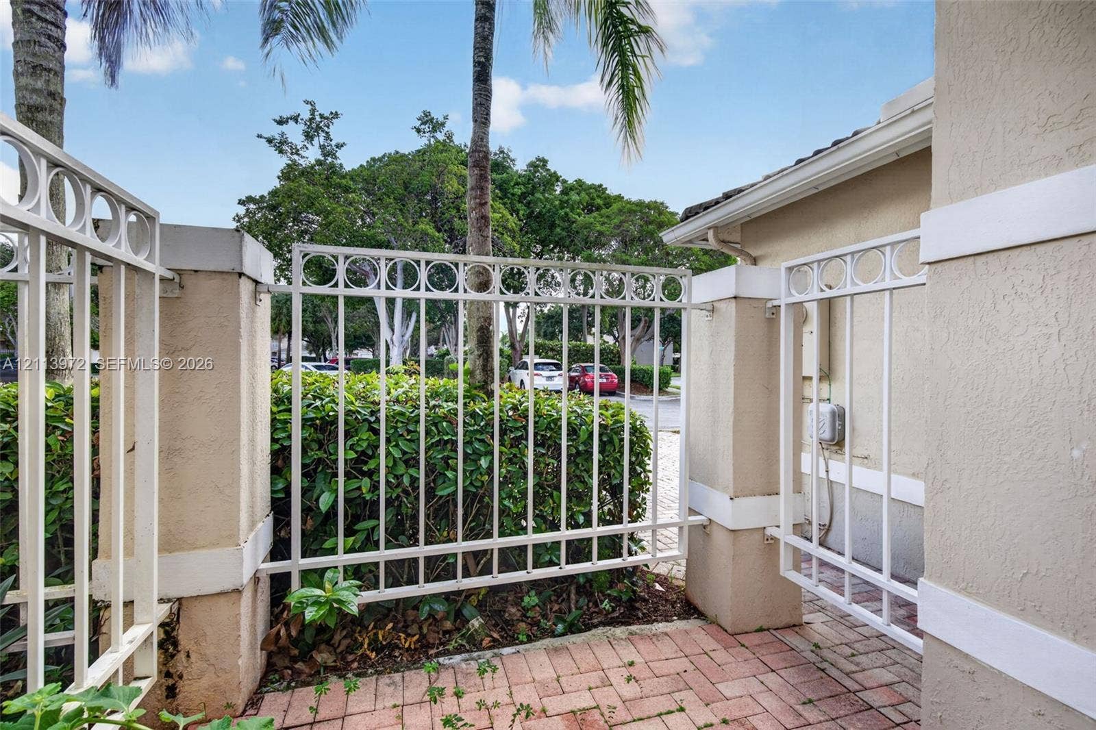 White metal fencing featuring a decorative circular pattern, stucco pillar accents, and a brick paver walkway