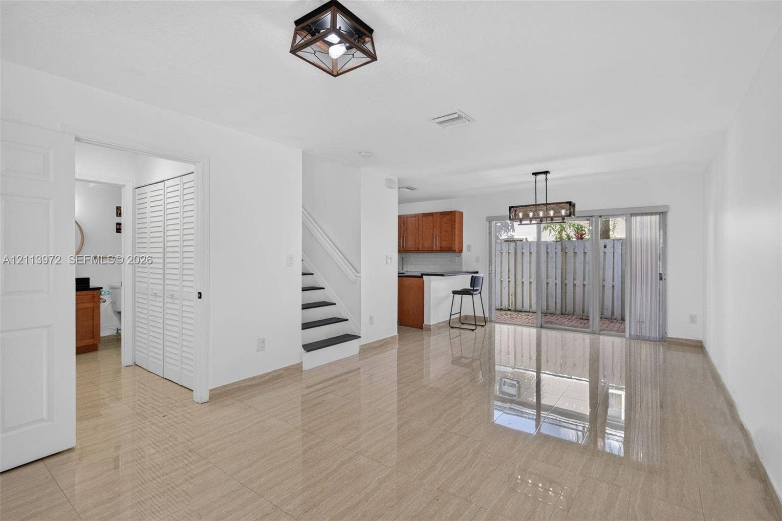 Open-concept interior featuring large-format tile flooring, a lantern-style flush mount ceiling light, an iron and glass chandelier, a staircase with contrast treads, and sliding glass doors