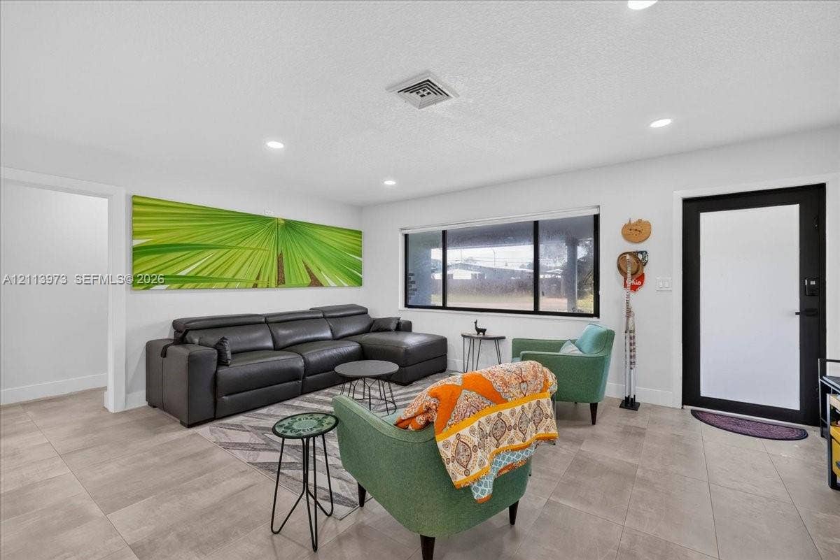 Neutral-toned large format tile flooring, recessed lighting, and a modern entry door featuring a matte black frame with frosted glass