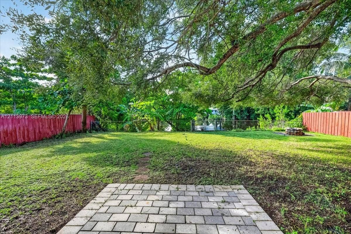 Private backyard featuring a paved stone patio, expansive lawn, mature tree canopy, and perimeter wood fencing