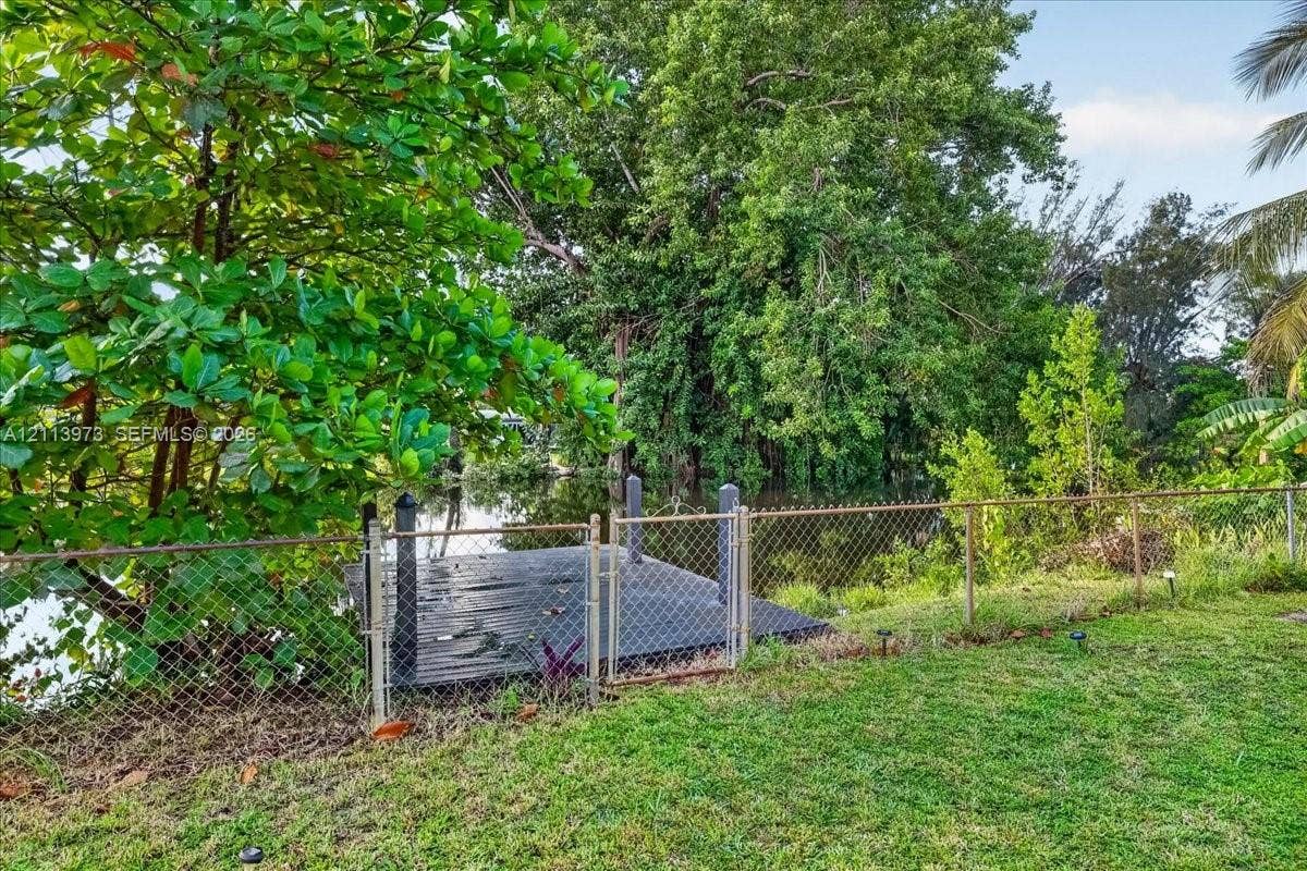 Waterfront property featuring a private wooden dock, chain-link perimeter fencing, and mature trees