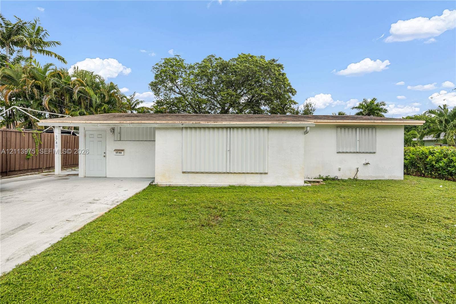 3740 NE 6th Avenue, Oakland Park, FL 33334 Single-story exterior featuring a light-toned facade, flat roofline, concrete driveway, and attached metal storm shutters
