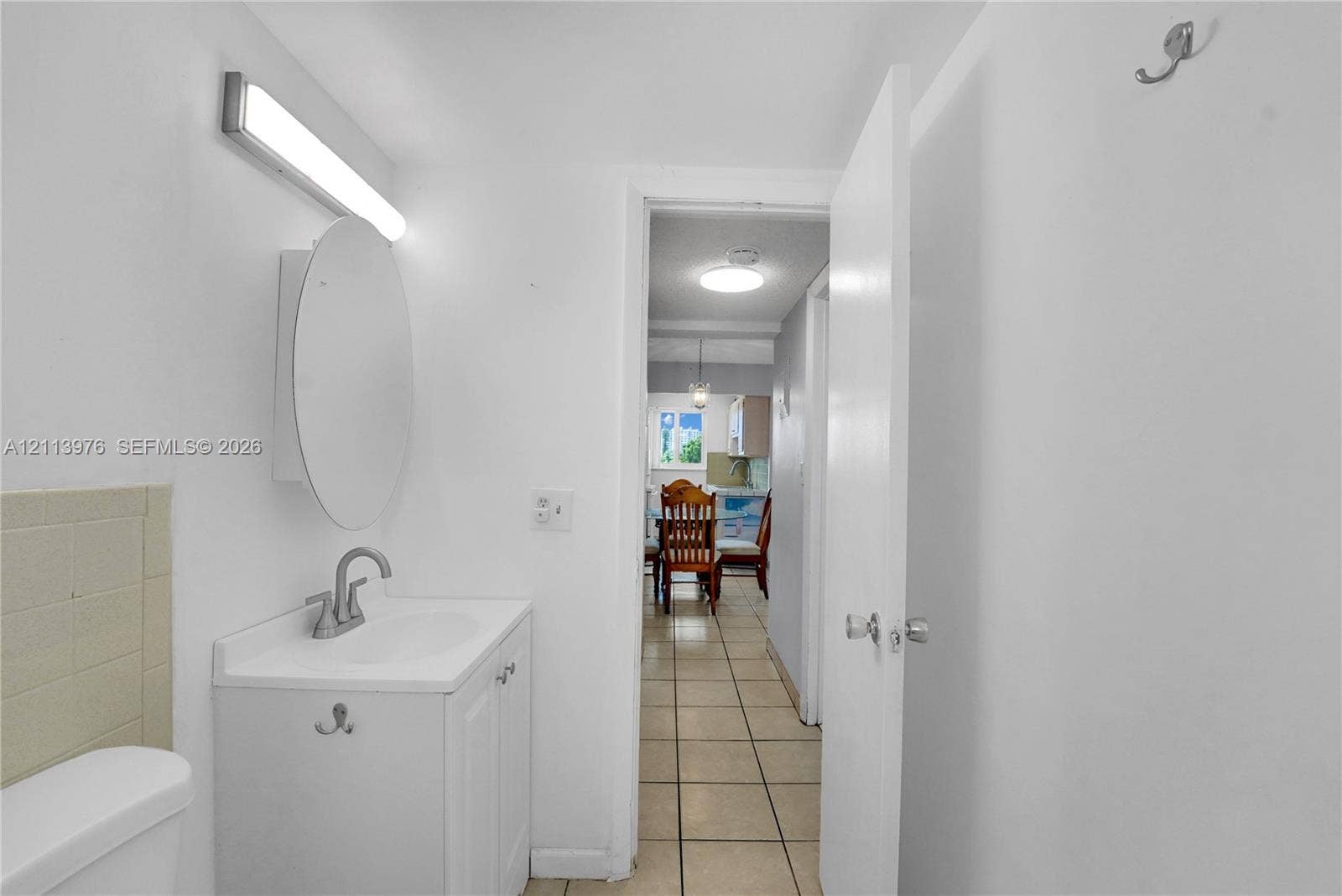 2145 Pierce Street, #416, Hollywood, FL 33020 White vanity with integrated sink, circular wall-mounted mirror, linear light fixture, ceramic tile flooring, and wall-mounted hardware