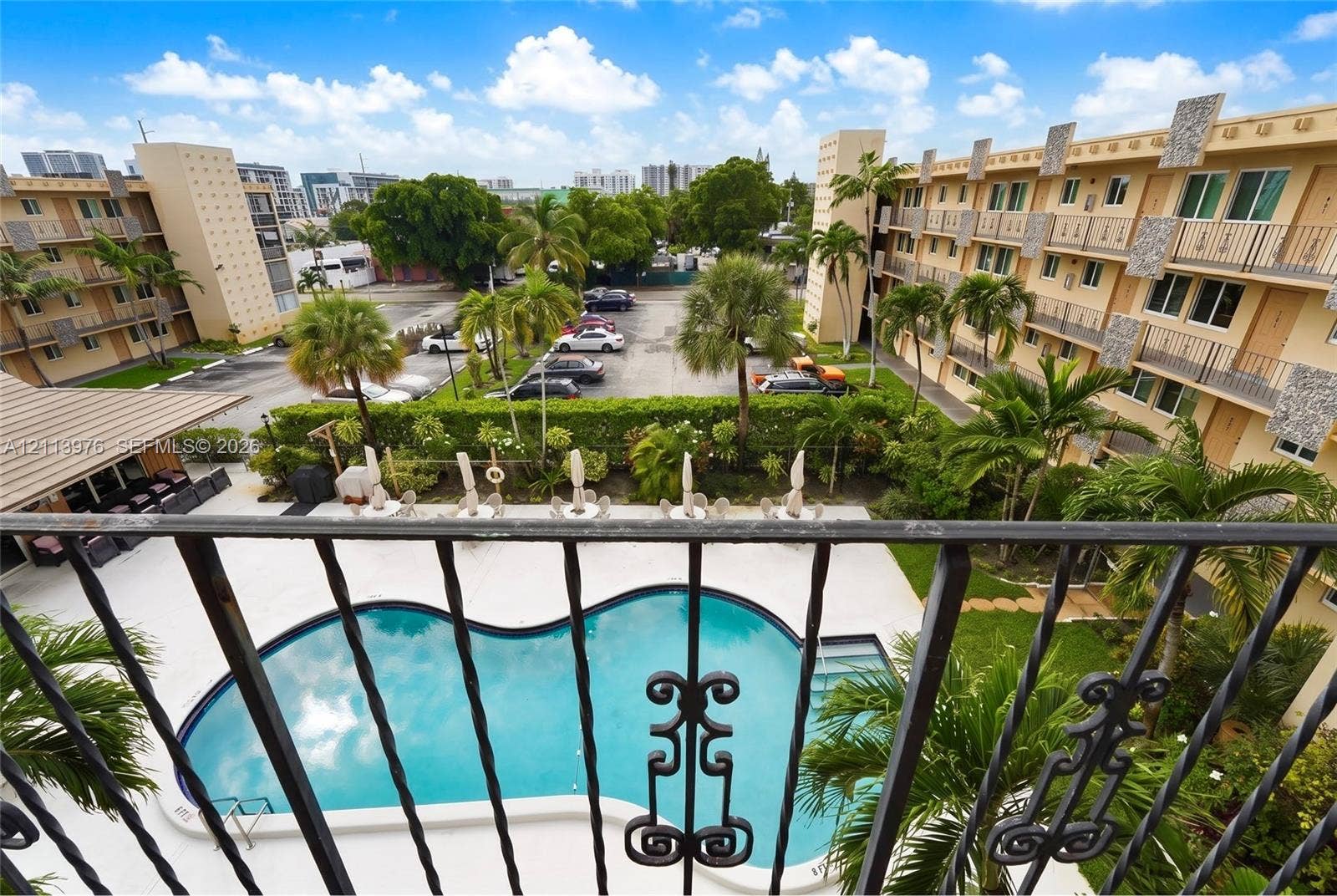 2145 Pierce Street, #416, Hollywood, FL 33020 Curved swimming pool, concrete pool deck, wrought iron balcony railing, mature palm trees, and multi-story building exterior