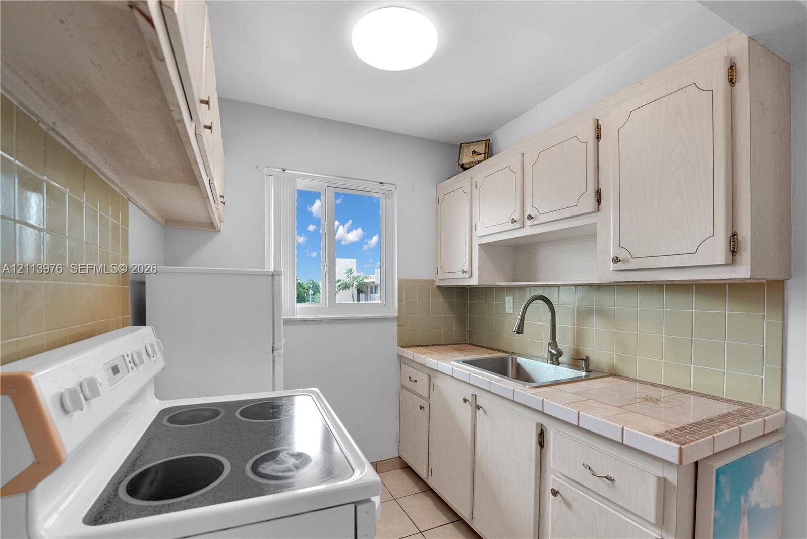 2145 Pierce Street, #416, Hollywood, FL 33020 Kitchen featuring light-toned cabinetry, tile countertops, tile backsplash, stainless steel sink with high-arc faucet, and a flush-mount ceiling light