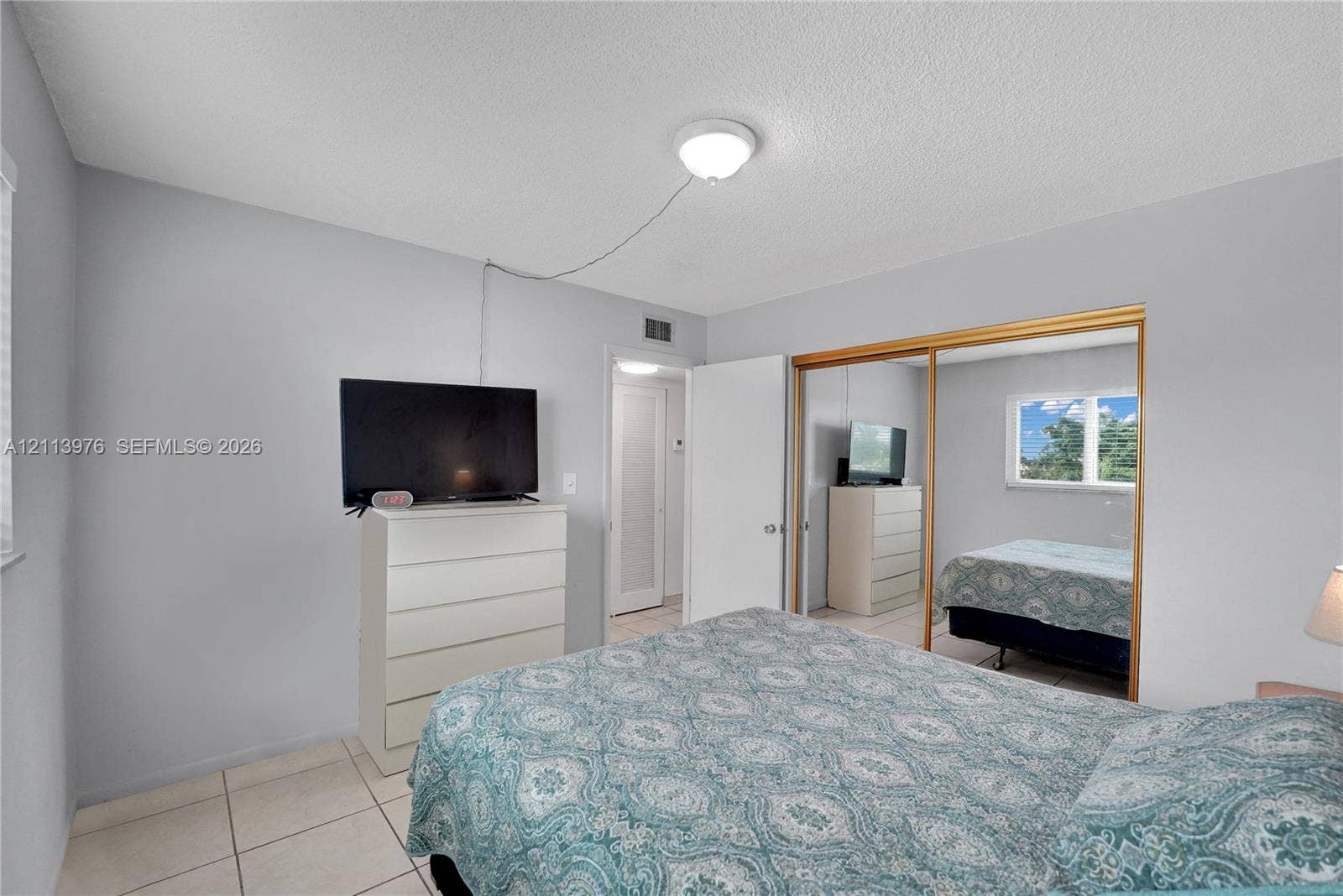 2145 Pierce Street, #416, Hollywood, FL 33020 Neutral-toned bedroom featuring tile flooring, sliding mirror-panel closet doors, and a ceiling-mounted light fixture
