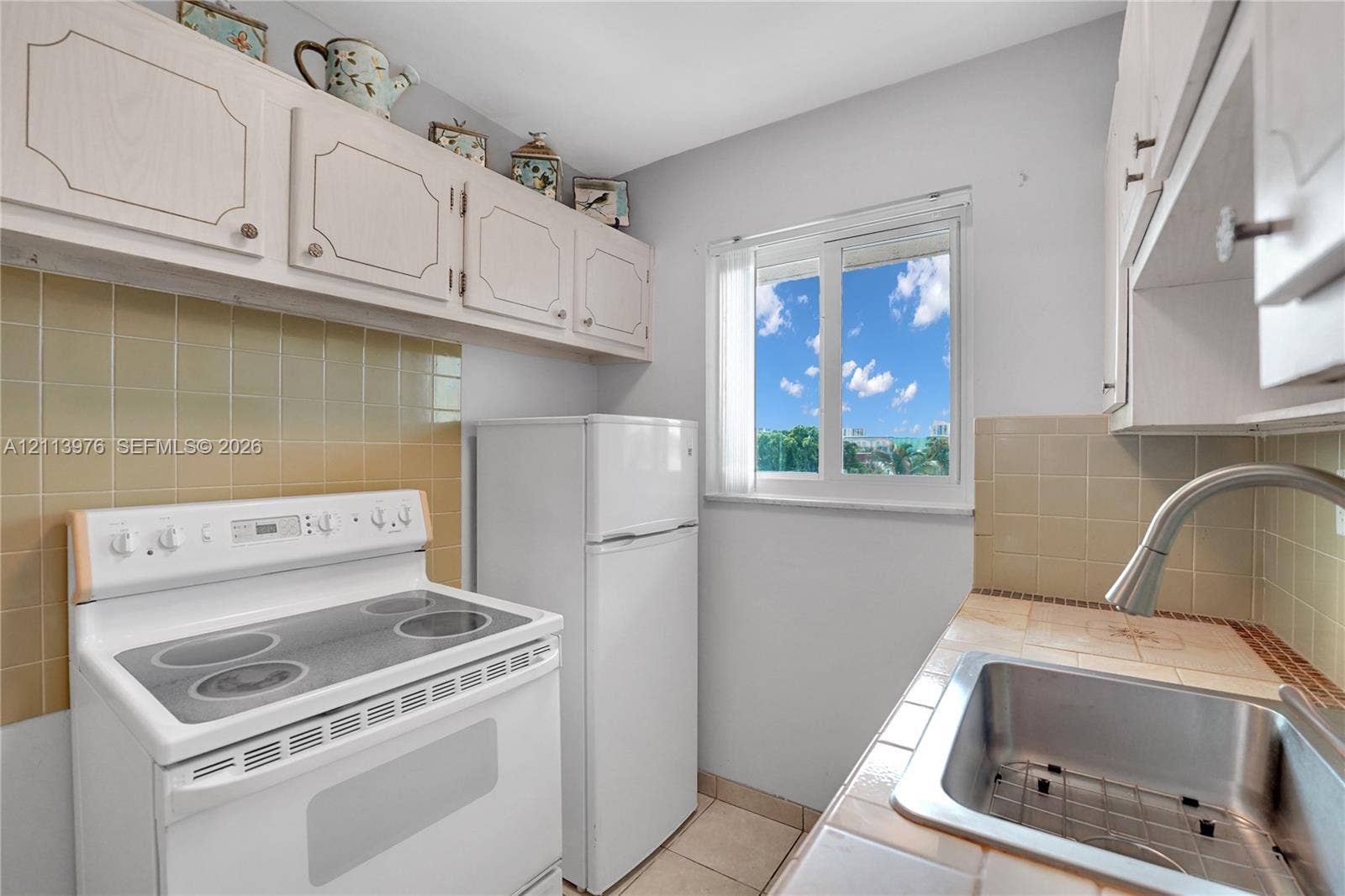 2145 Pierce Street, #416, Hollywood, FL 33020 Kitchen featuring white cabinetry, tile backsplash, stainless steel sink with high-arc faucet, electric range, and tile flooring