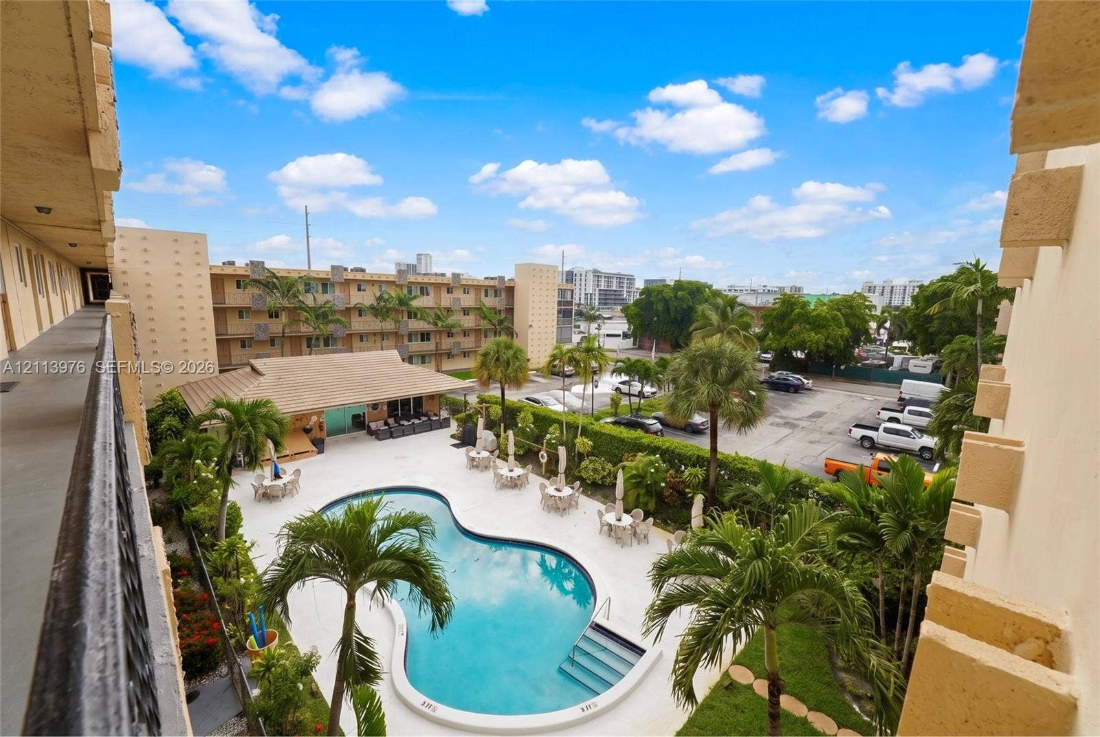 2145 Pierce Street, #416, Hollywood, FL 33020 Community pool area featuring a free-form swimming pool, paved sundeck, lush landscaping with mature palm trees, and an attached covered cabana