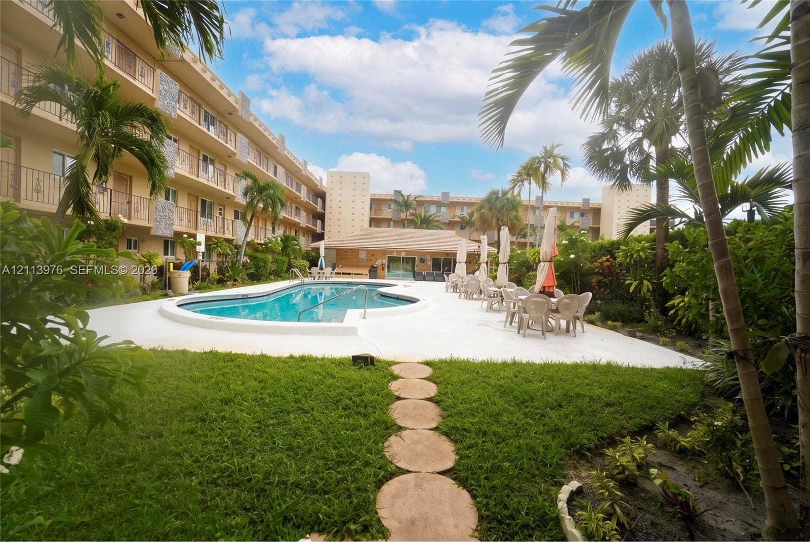 2145 Pierce Street, #416, Hollywood, FL 33020 Swimming pool area featuring a concrete deck, stepping stone walkway, manicured lawn, and mature palm trees