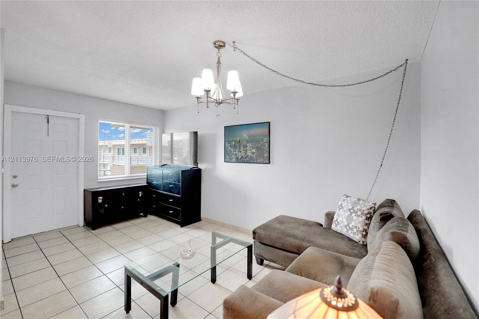 2145 Pierce Street, #416, Hollywood, FL 33020 Interior room featuring neutral wall tones, large-format tile flooring, a multi-arm chandelier with chain-link suspension, and a window providing natural light