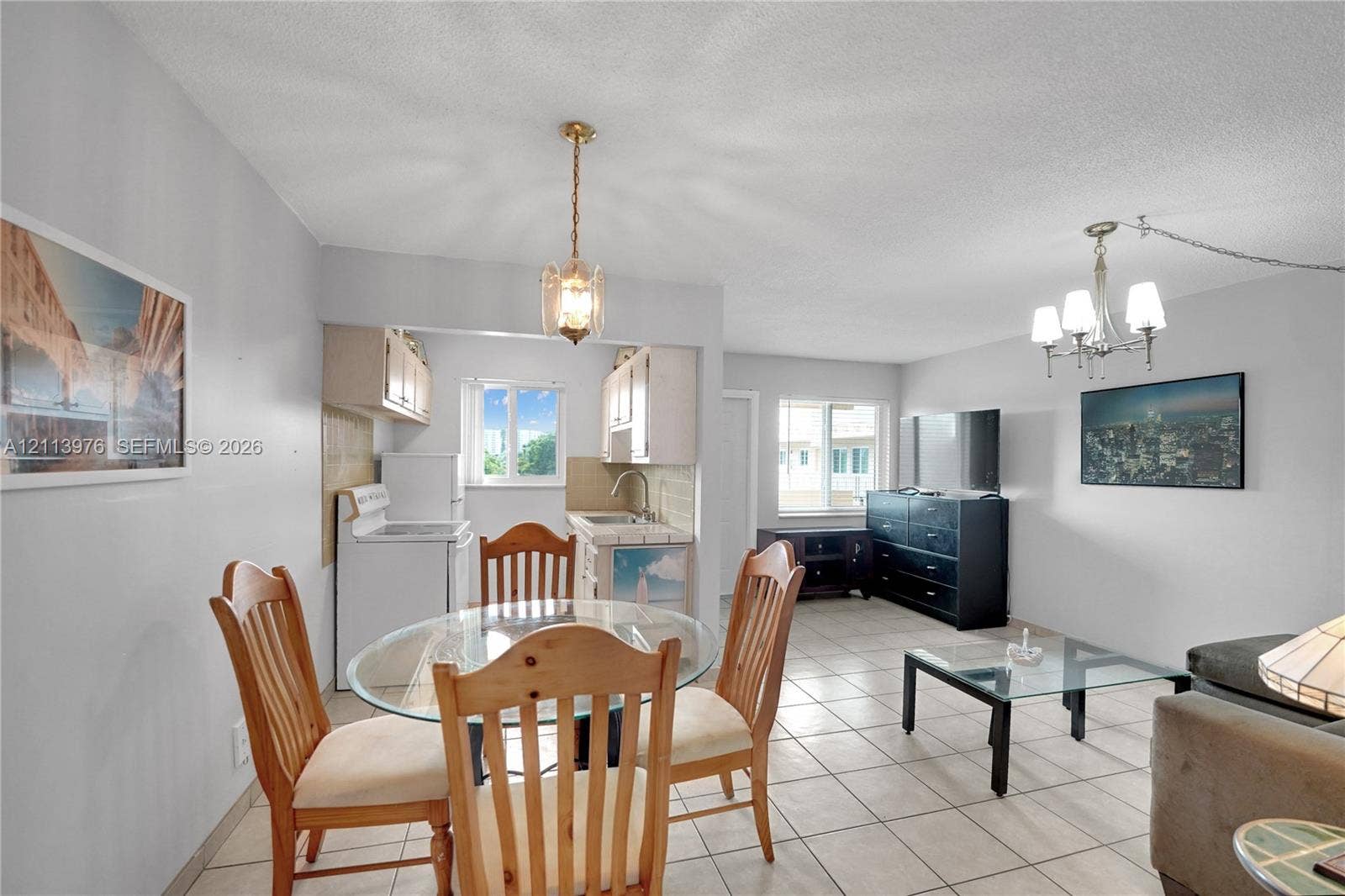 2145 Pierce Street, #416, Hollywood, FL 33020 Kitchen area featuring tile countertops, white cabinetry, and a single-basin stainless steel sink, complemented by neutral tile flooring throughout and dual multi-arm metal chandeliers