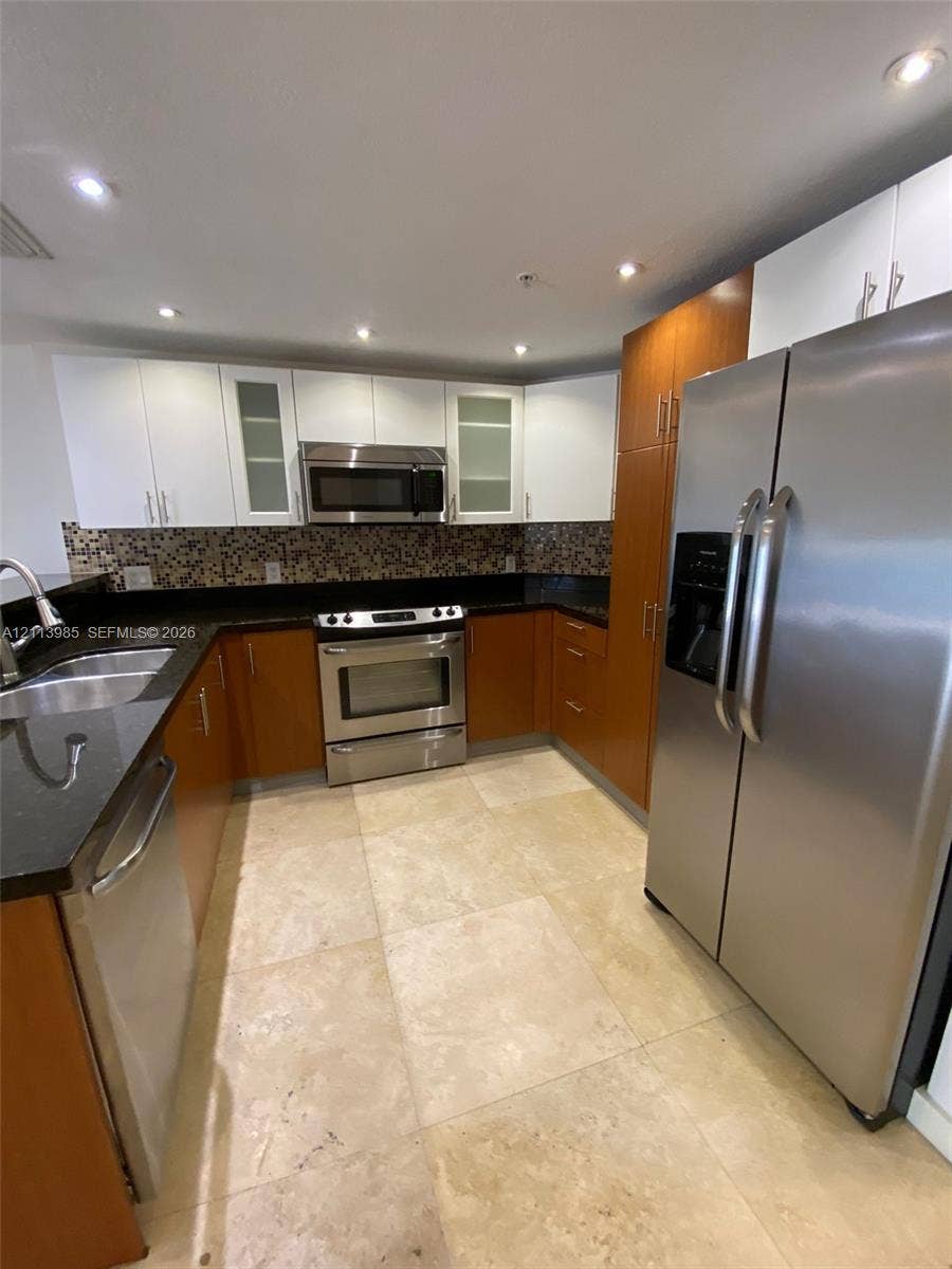 170 SE 14th Street, #2203, Miami, Miami, FL 33131 Kitchen featuring two-tone cabinetry, stainless steel appliances, dark stone countertops, mosaic tile backsplash, and light-toned tile flooring