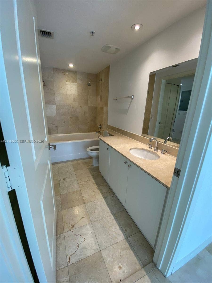 170 SE 14th Street, #2203, Miami, Miami, FL 33131 Bathroom featuring large-format tile flooring, tile surround bathtub, white cabinetry, integrated countertop with oval sink, and a wall-mounted mirror