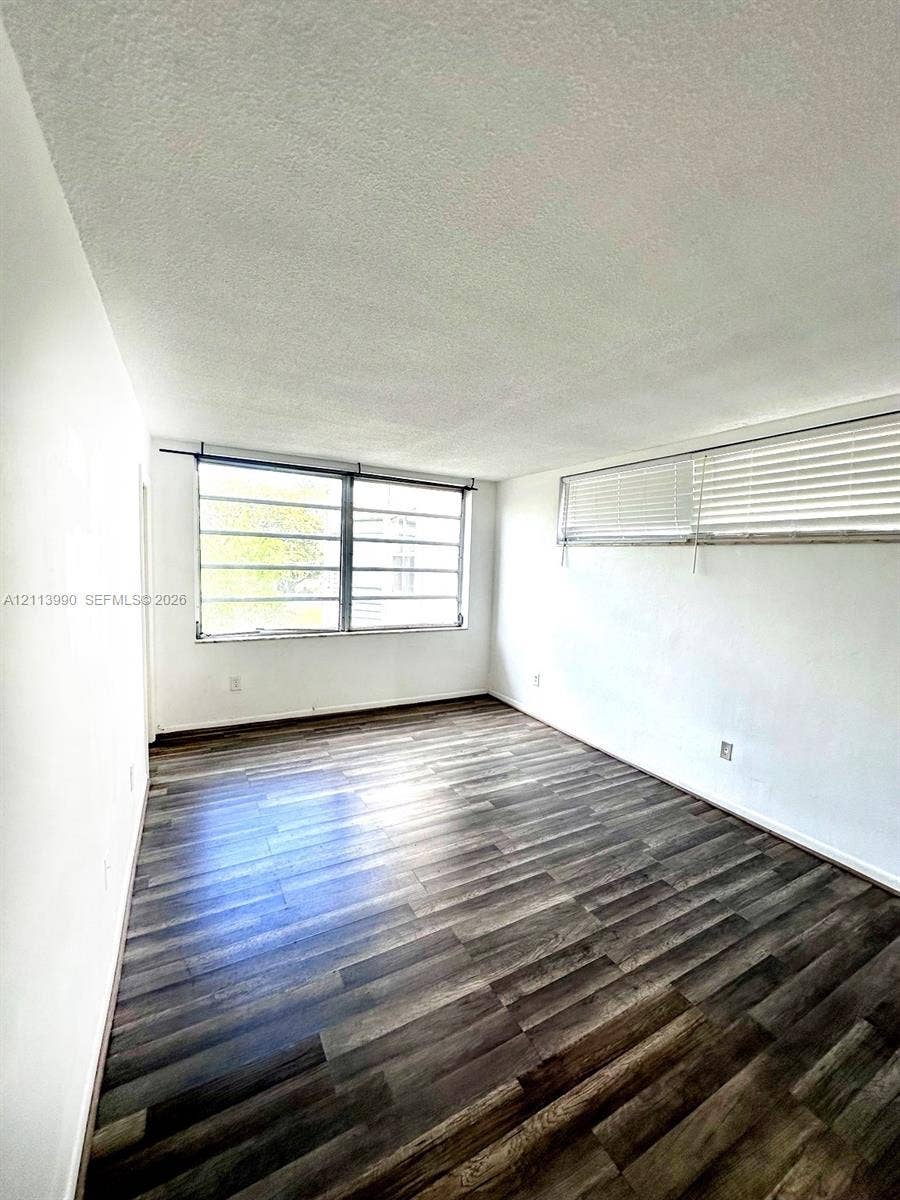 1501 NE 191st Street, #C312, Miami, FL 33179 Interior space featuring wood-finish flooring, white walls, and multi-pane windows with horizontal blinds