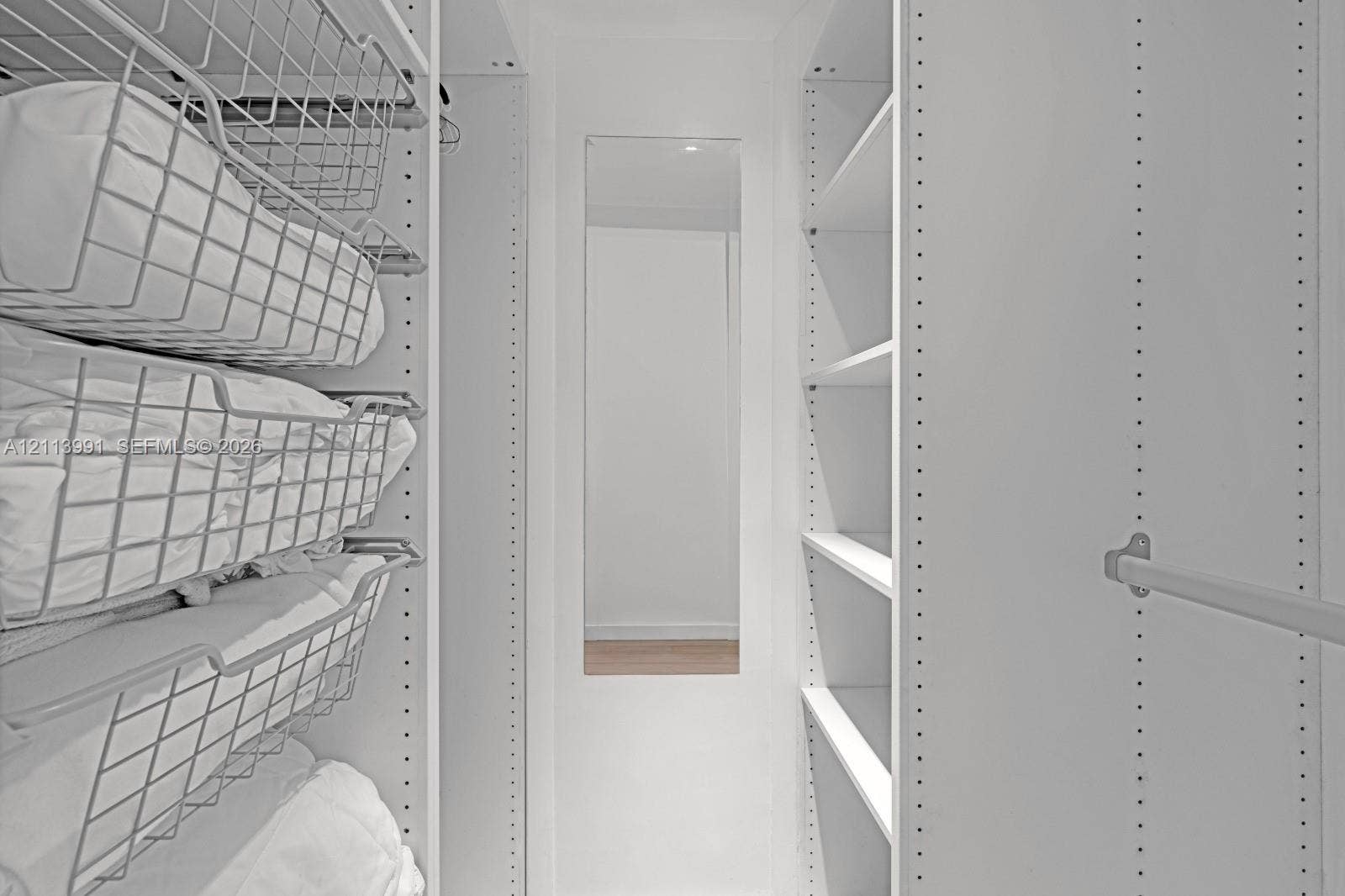 Custom white closet system featuring adjustable shelving, integrated wire pull-out baskets, a full-length mirror, and horizontal hanging rods