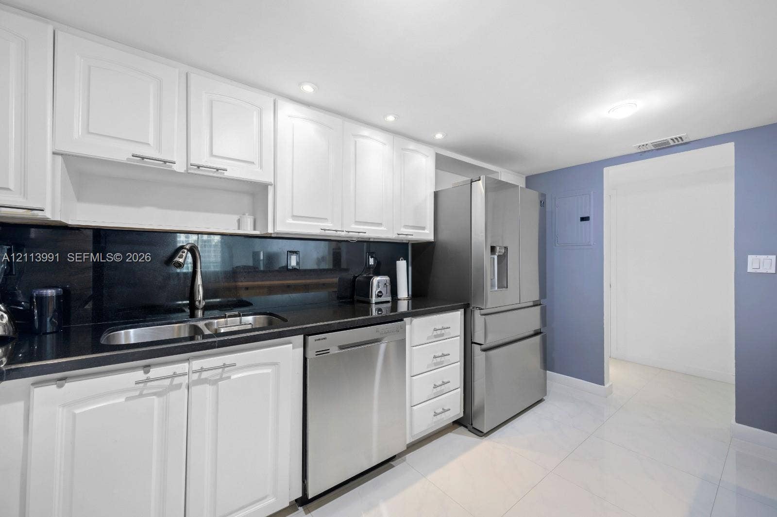 Kitchen featuring white cabinetry, dark stone countertops, stainless steel appliances, a dual-basin undermount sink, and polished tile flooring