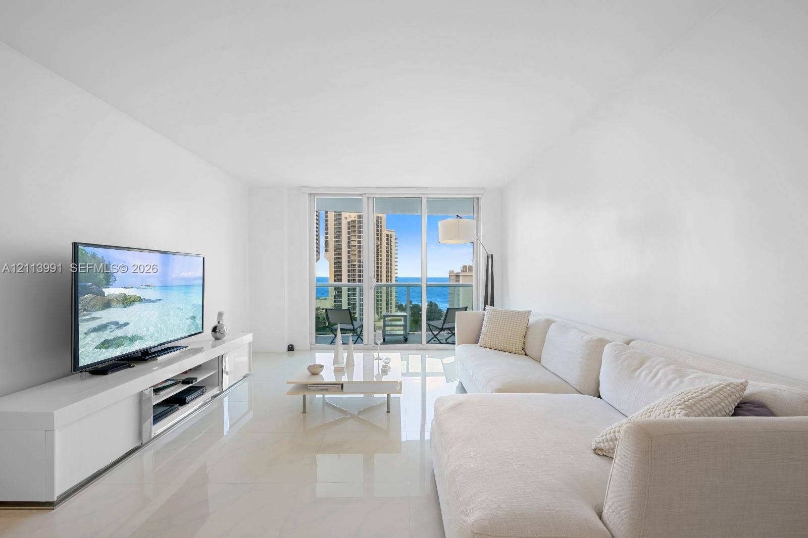 Living area featuring polished stone flooring, floor-to-ceiling glass sliding doors, and a glass-paneled balcony