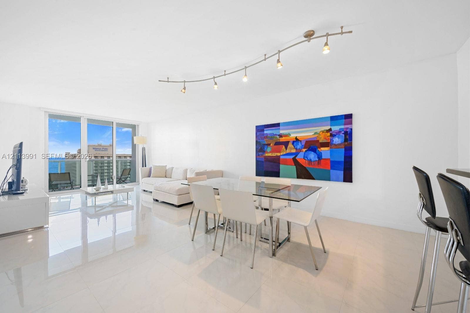 Open-concept room featuring light-toned tile flooring, recessed curved track lighting, and floor-to-ceiling glass sliding doors