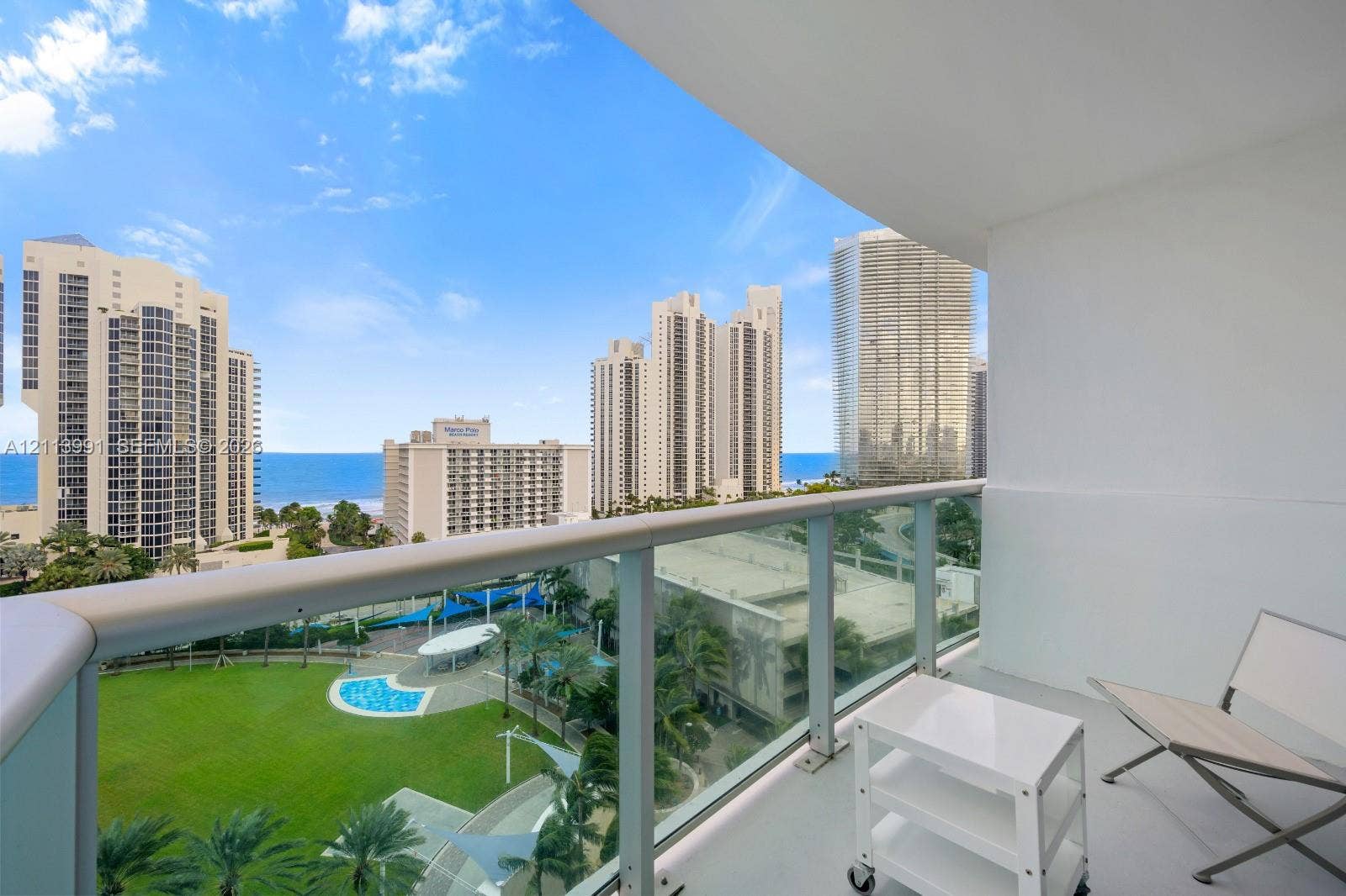 Private balcony with glass panel railing, concrete flooring, and panoramic coastal and urban scenery