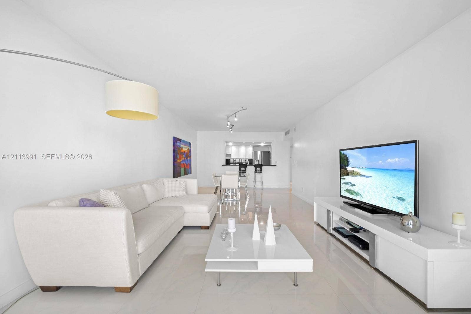 Open-concept interior featuring light-toned tile flooring, recessed track lighting, and a breakfast bar pass-through