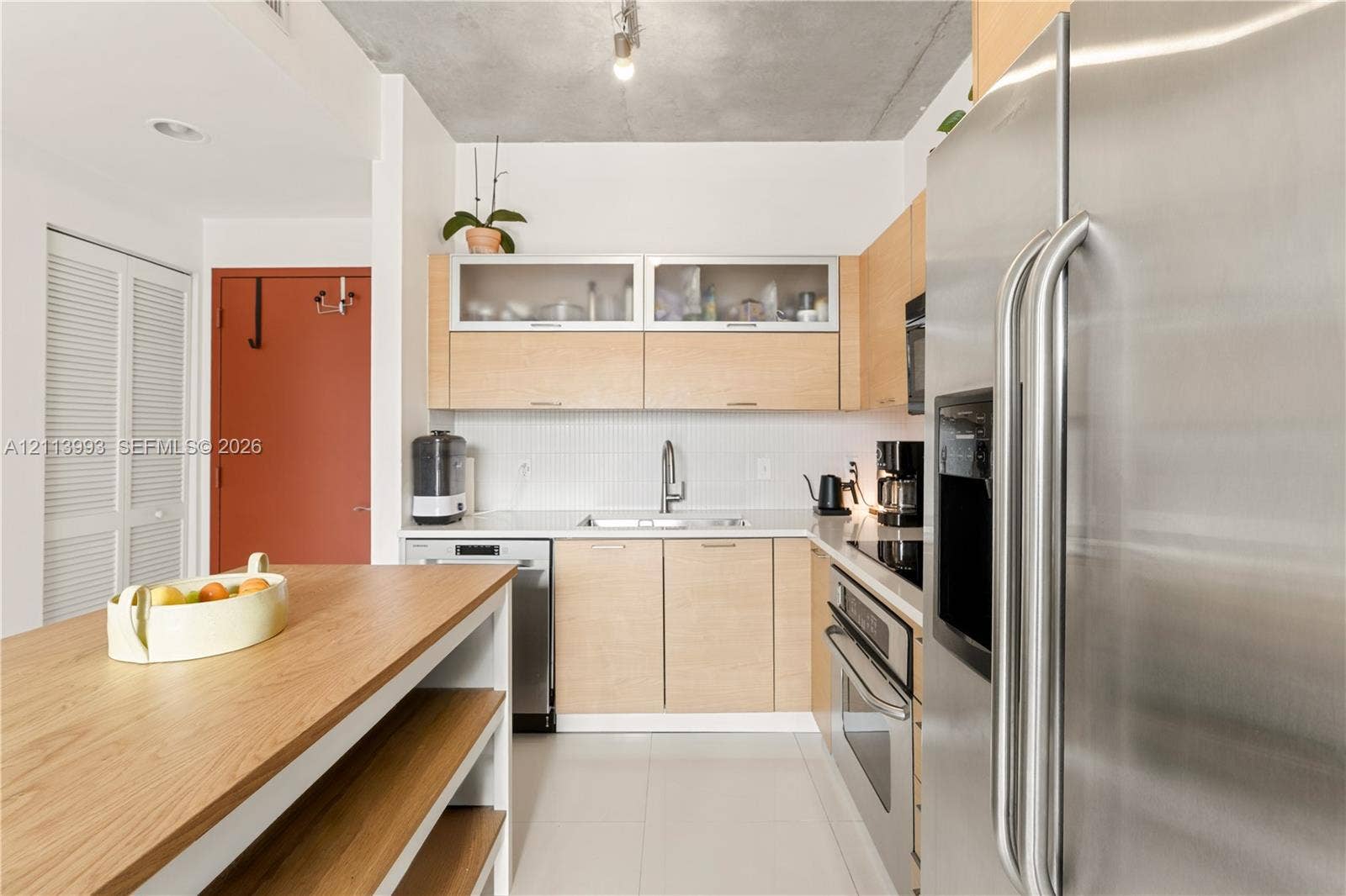 3180 SW 22nd Terrace, #407, Miami, Miami, FL 33145 Kitchen featuring light wood-finish cabinetry, stainless steel appliances, white tile backsplash, exposed concrete ceiling, and a built-in island with open shelving