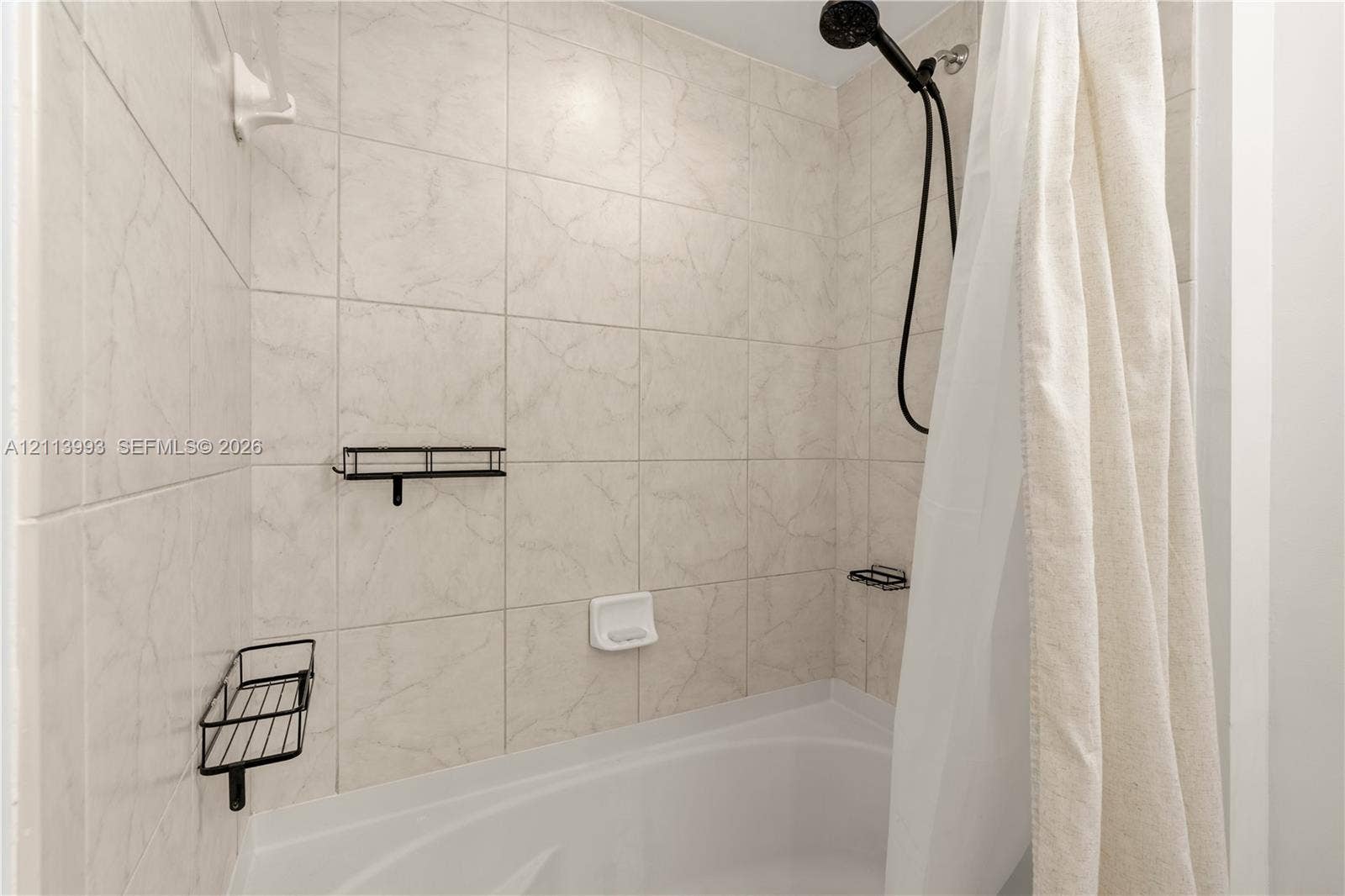 3180 SW 22nd Terrace, #407, Miami, Miami, FL 33145 Bathtub enclosure featuring neutral tile wall surround, black finish handheld shower head, and dual black wire wall-mounted storage caddies
