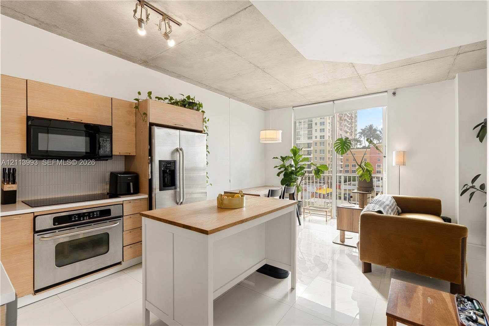 3180 SW 22nd Terrace, #407, Miami, Miami, FL 33145 Kitchen featuring light wood-finish cabinetry, stainless steel appliances, a white center island with a wood-finish surface, polished flooring, and exposed concrete ceilings