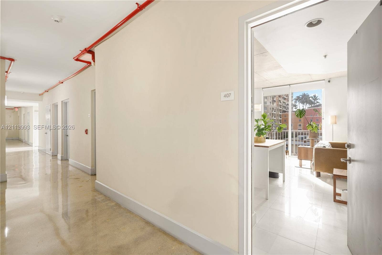 3180 SW 22nd Terrace, #407, Miami, Miami, FL 33145 Interior hallway featuring polished concrete flooring, exposed red fire suppression piping, and tile flooring within the doorway