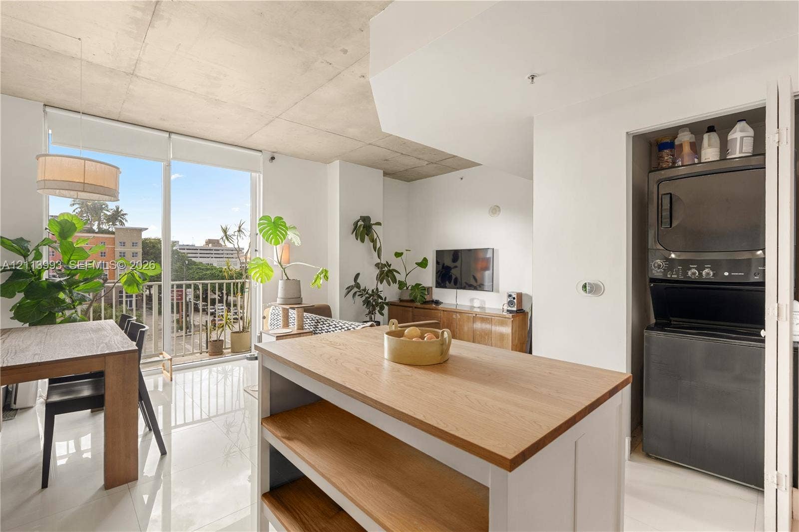 3180 SW 22nd Terrace, #407, Miami, Miami, FL 33145 Open-concept interior featuring high exposed concrete ceilings, floor-to-ceiling glass paneling, polished tile flooring, a kitchen island with a wood countertop, and a built-in stackable laundry unit