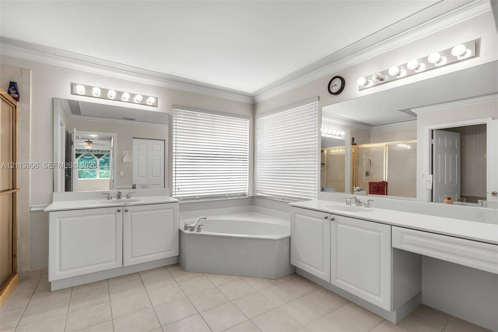 15503 SW 19th Street, Miramar, FL 33027 Dual white cabinetry vanities with inset-panel doors, solid surface countertops, corner soaking tub, ceramic tile flooring, and oversized wall-to-wall mirrors