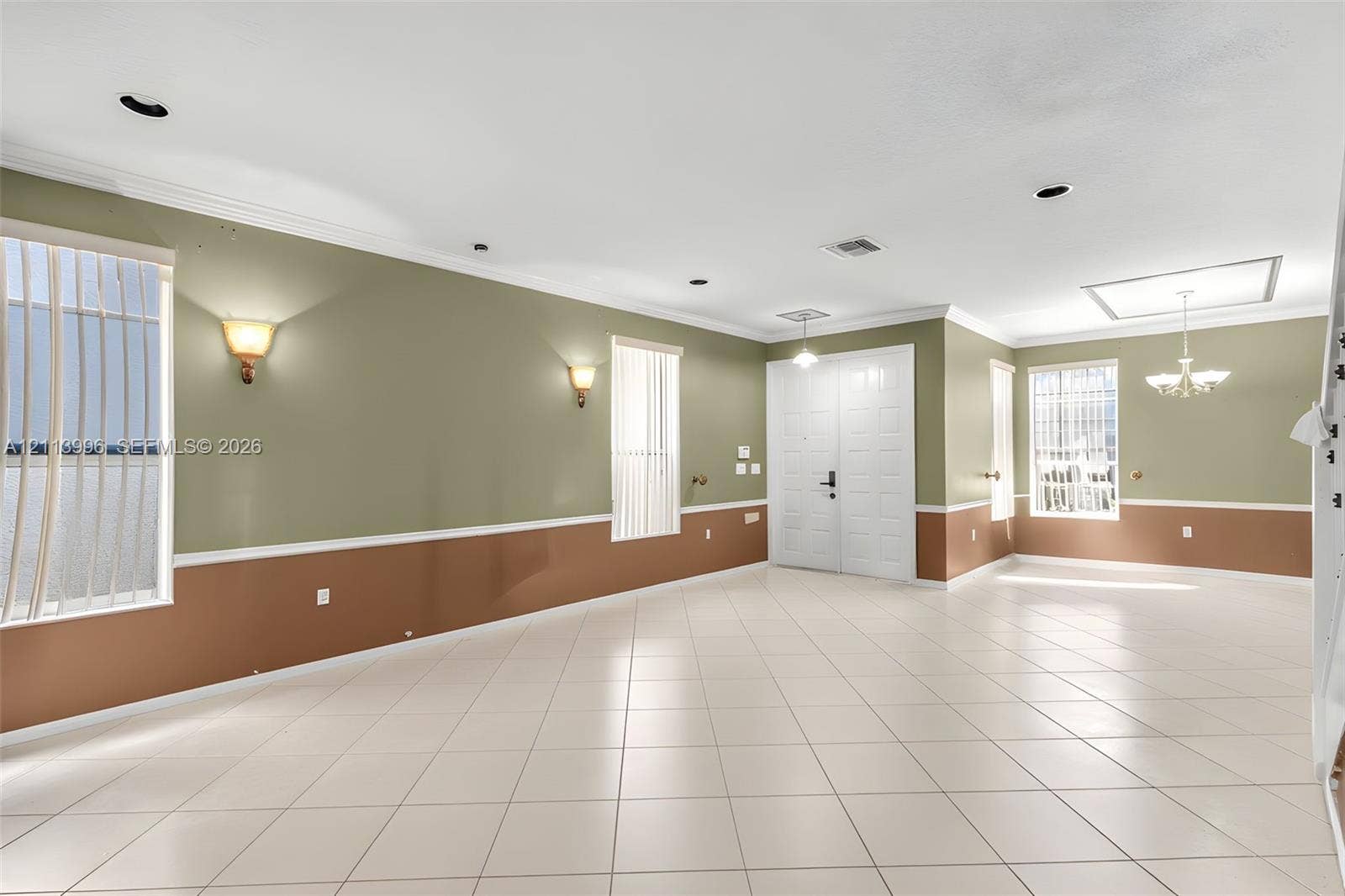 15503 SW 19th Street, Miramar, FL 33027 Open-concept interior featuring light tile flooring, crown molding, double-door entryway, dual wall-mounted sconce lighting, and a multi-arm chandelier