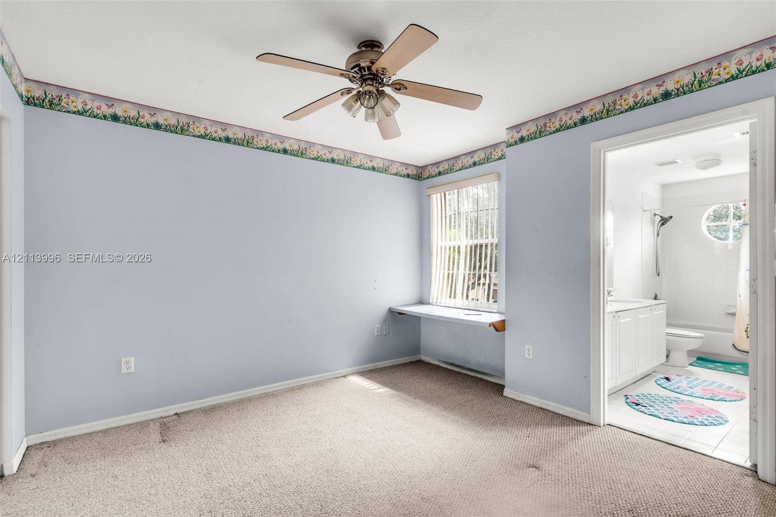 15503 SW 19th Street, Miramar, FL 33027 Room featuring neutral carpeting, a ceiling fan with light fixture, a built-in wall desk beneath a window, and a doorway to a bathroom