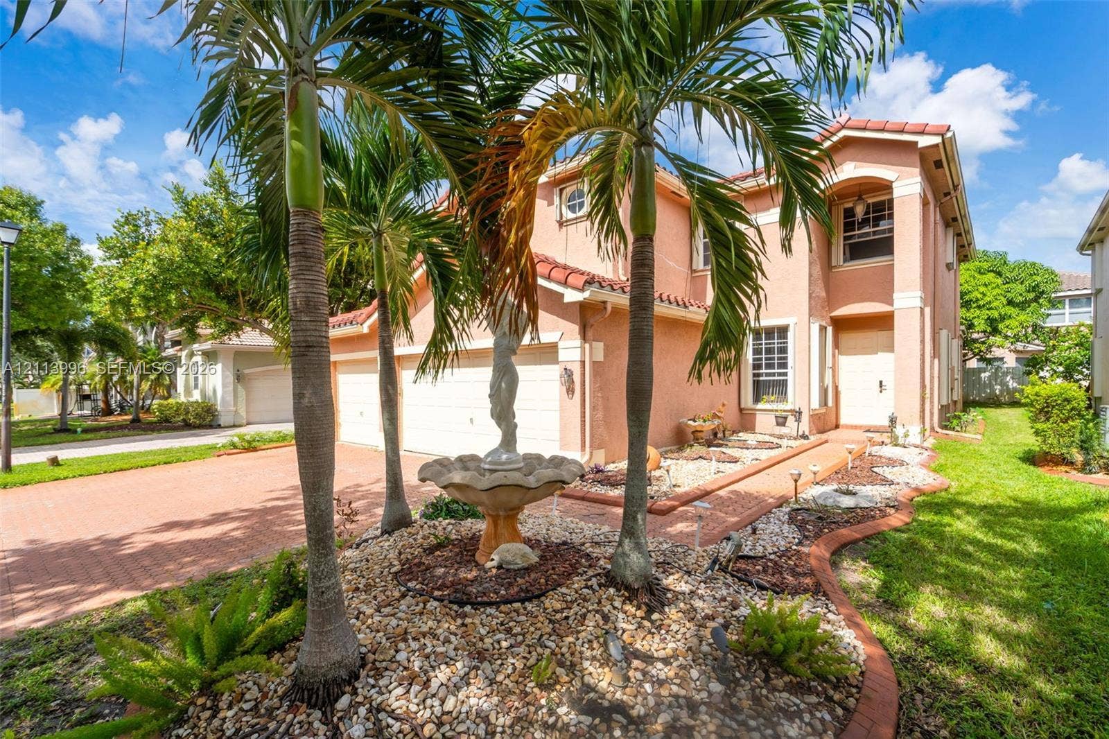 15503 SW 19th Street, Miramar, FL 33027 Two-story exterior featuring a stucco facade, red tile roof, multi-car garage, paver driveway, and front garden with a central fountain