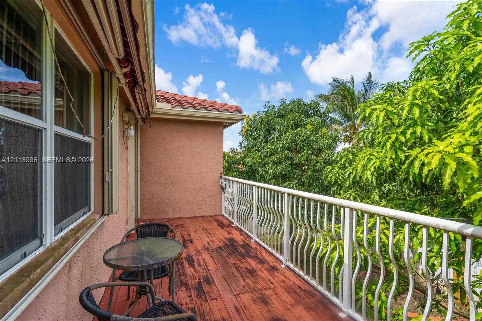 15503 SW 19th Street, Miramar, FL 33027 Exterior balcony featuring red-toned wood-finish decking, white metal balustrades, stucco wall cladding, and a red tile roofline