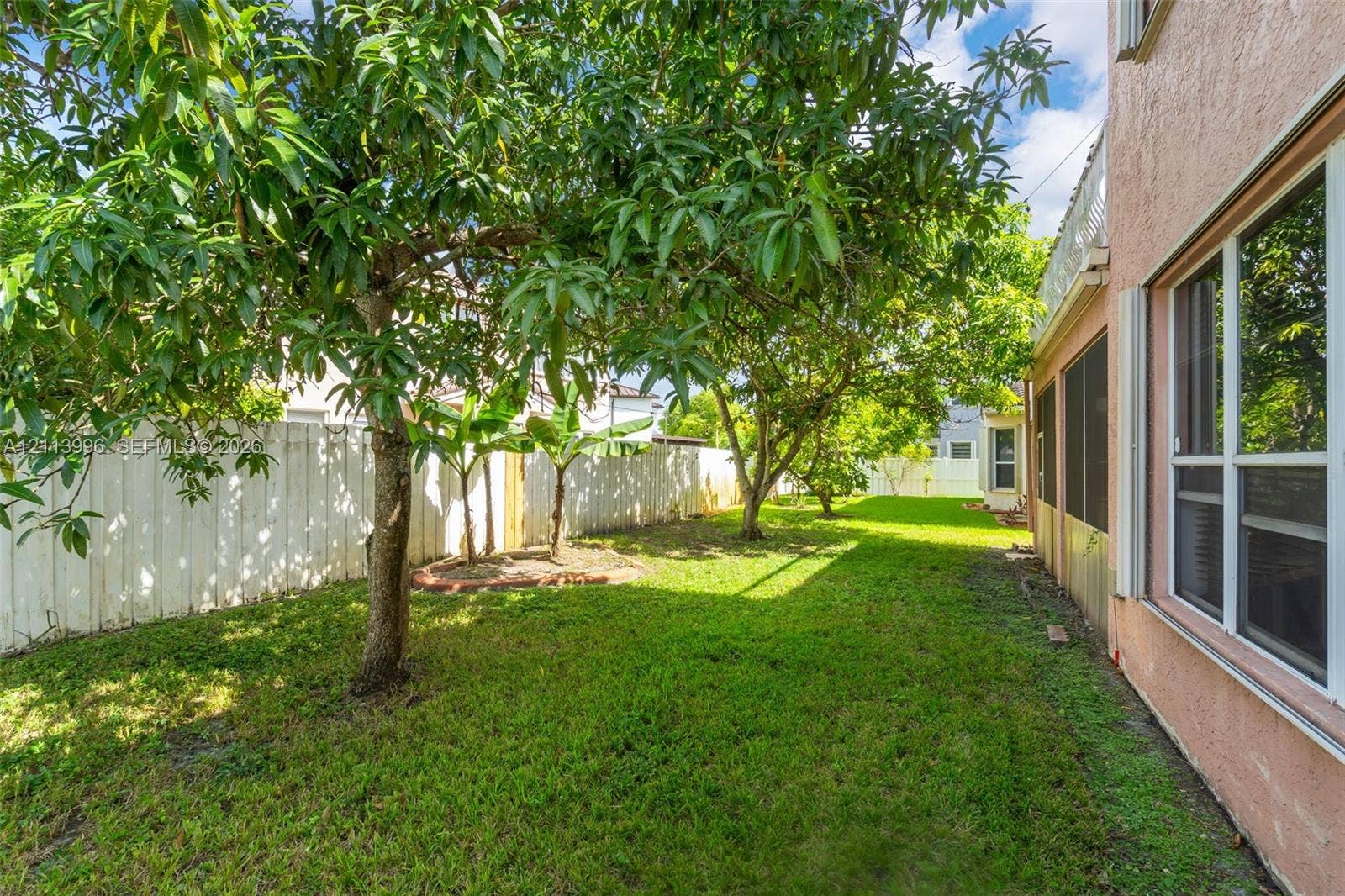 15503 SW 19th Street, Miramar, FL 33027 Backyard featuring mature trees, a manicured lawn, a white privacy fence, and an exterior screen enclosure