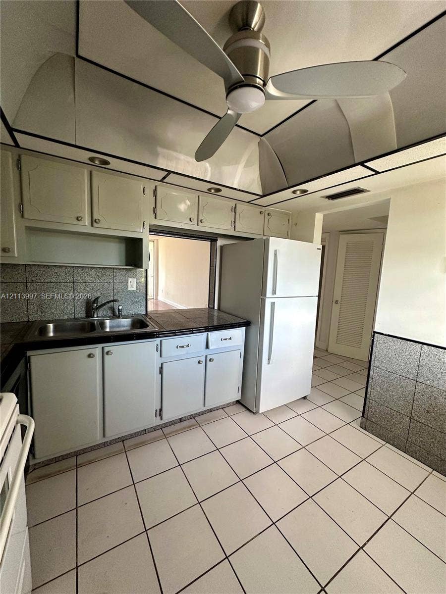 1501 NE 191st Street, #C412, Miami, FL 33179 Kitchen featuring custom cabinetry, tile backsplash, built-in ceiling fan, and tiled flooring