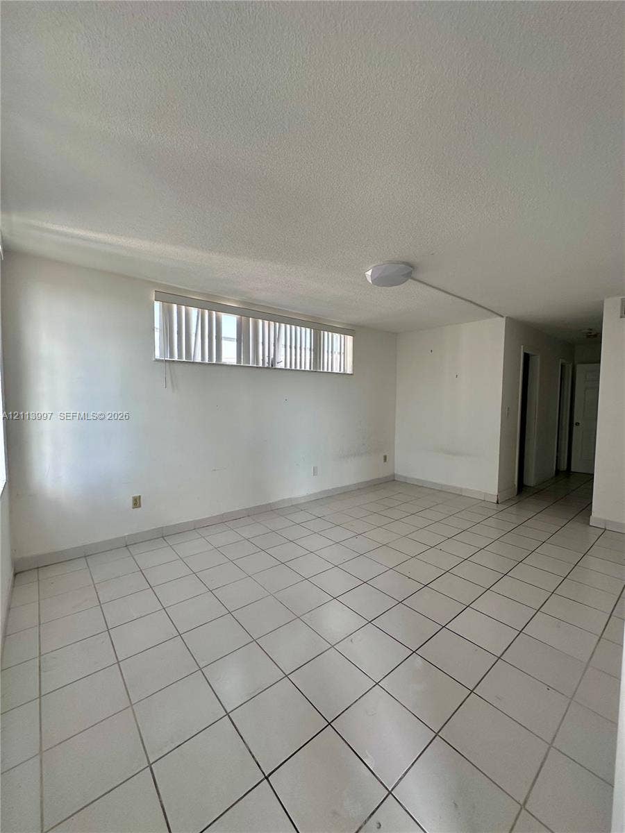 1501 NE 191st Street, #C412, Miami, FL 33179 Neutral interior featuring white tile flooring, white walls, a horizontal clerestory-style window with vertical blinds, and a central ceiling-mounted light fixture