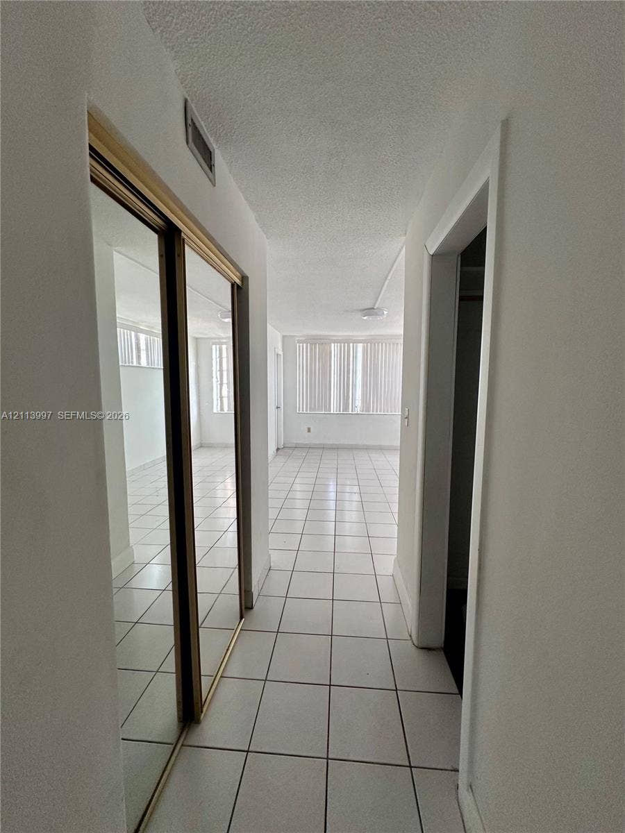 1501 NE 191st Street, #C412, Miami, FL 33179 Hallway featuring large-format ceramic tile flooring, floor-to-ceiling mirrored closet doors, and smooth-finish ceilings