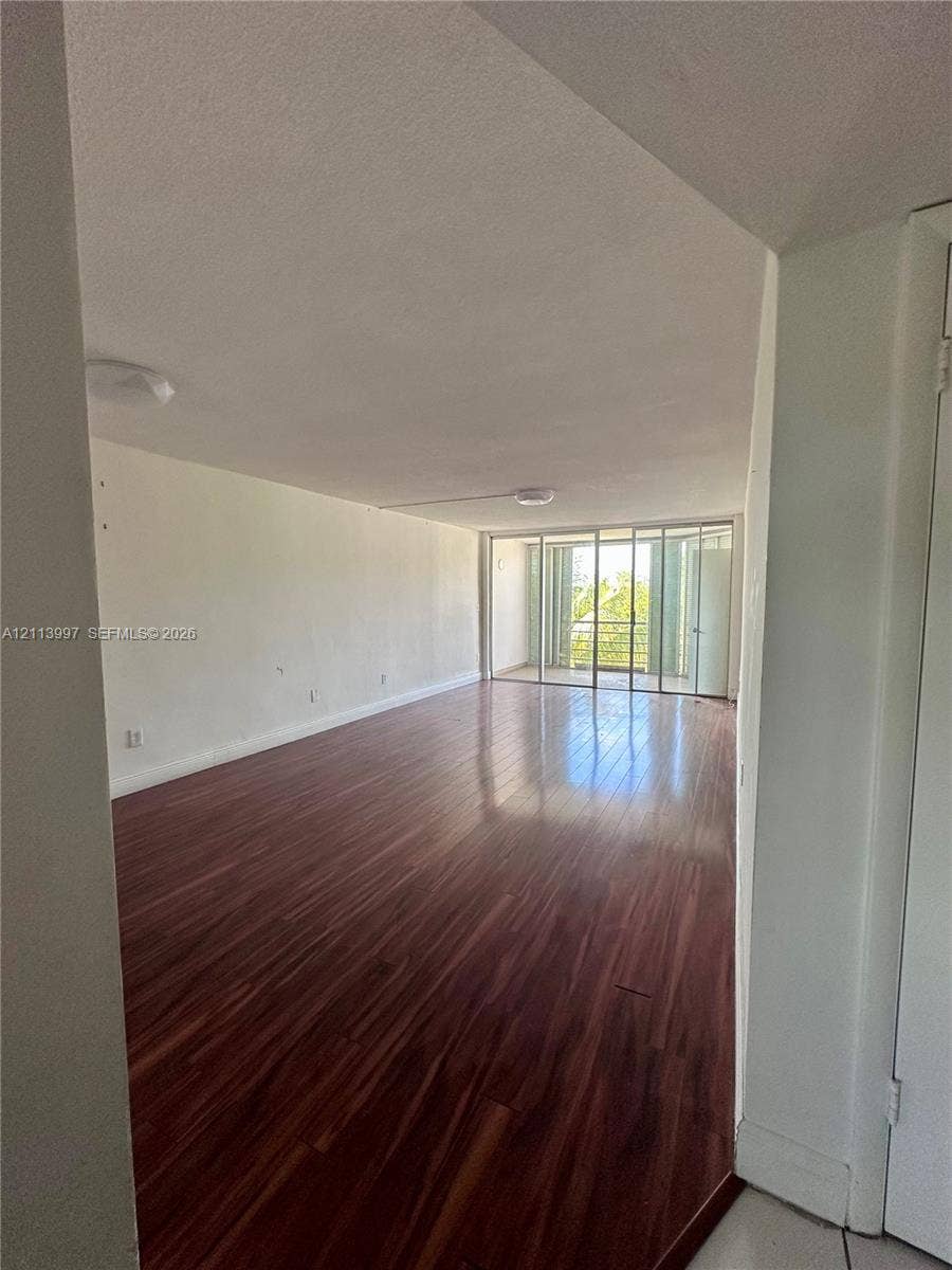 1501 NE 191st Street, #C412, Miami, FL 33179 Open interior space featuring wood-finish flooring, ceiling-mounted light fixtures, and floor-to-ceiling glass sliding doors opening to a balcony