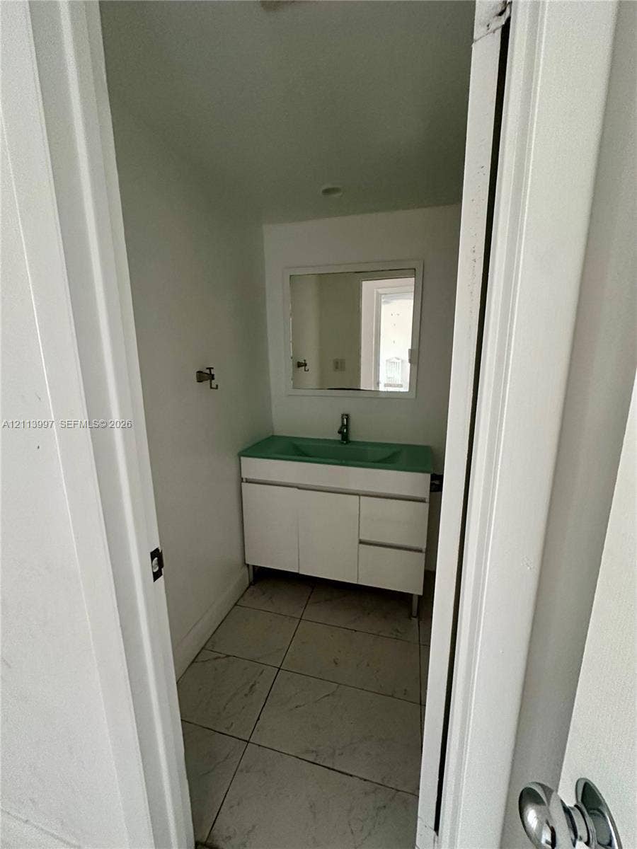 1501 NE 191st Street, #C412, Miami, FL 33179 White vanity with integrated colored sink, rectangular wall-mounted mirror, and large-format tile flooring