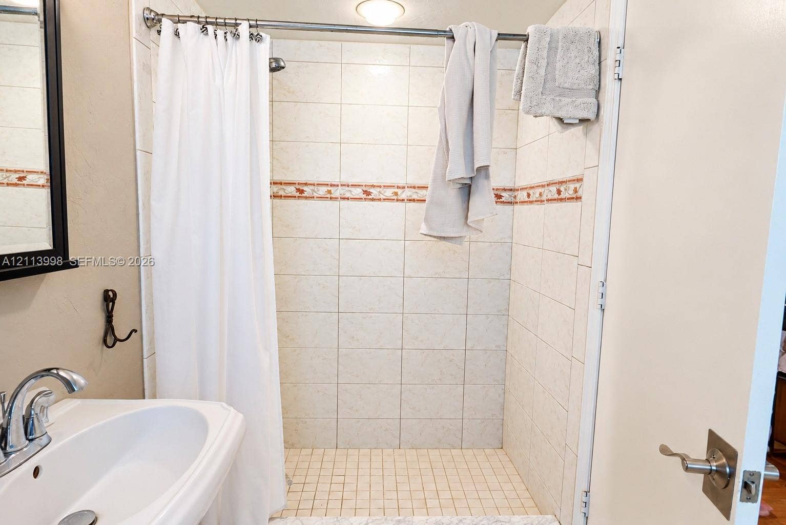 16455 SW 91st Avenue, Palmetto Bay, FL 33157 Bathroom featuring a wall-mounted sink with a chrome finish faucet, a tile-surround shower with an integrated decorative accent border, and a square tile shower floor